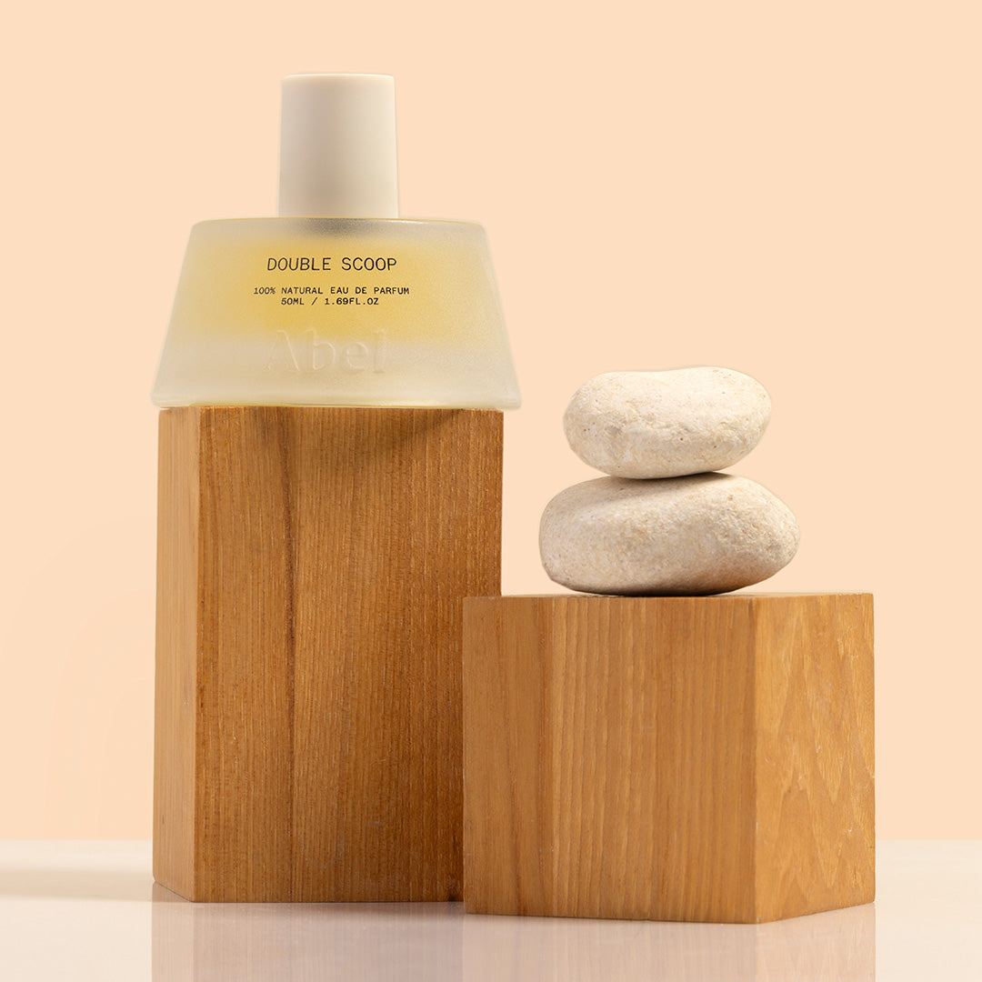 Abel | Double Scoop | Styled Image | Frosted glass fragrance bottle with white cap sitting on top of a wood block