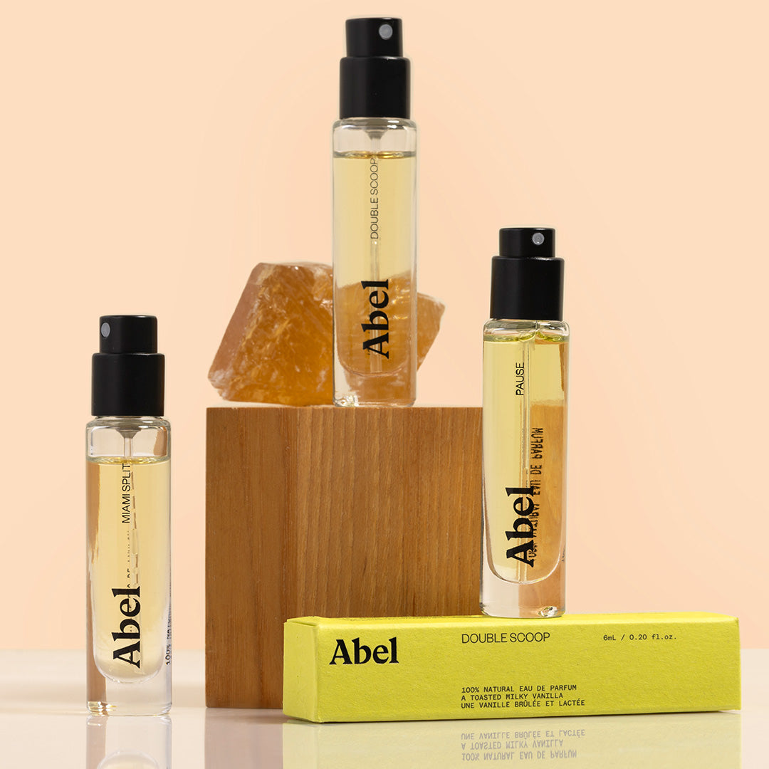 Abel | Fragance 6 ml Travel Size | Styled image of three 6 ml travel size clear glass perfume bottles with black spray tops and one lime green box