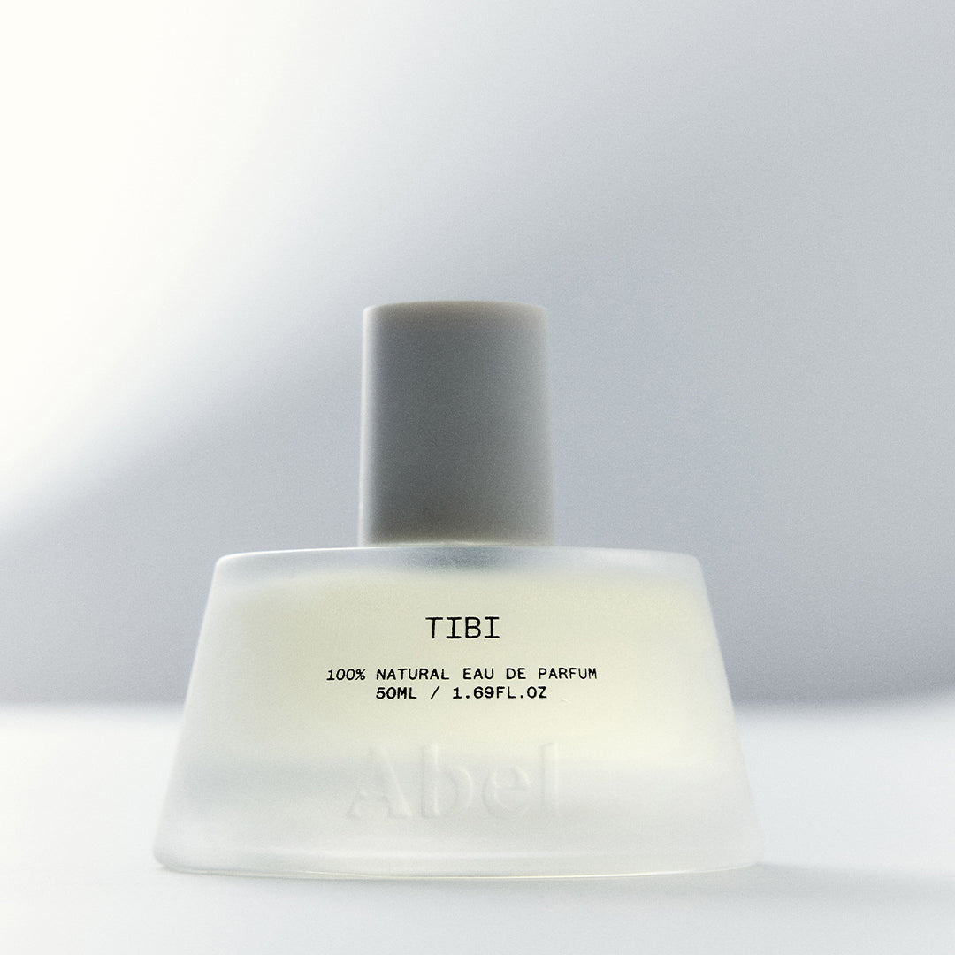 Abel | Tibi 50 ml | Lifestyle Image - frosted glass bottle with a cream cap against a softly lit gray background