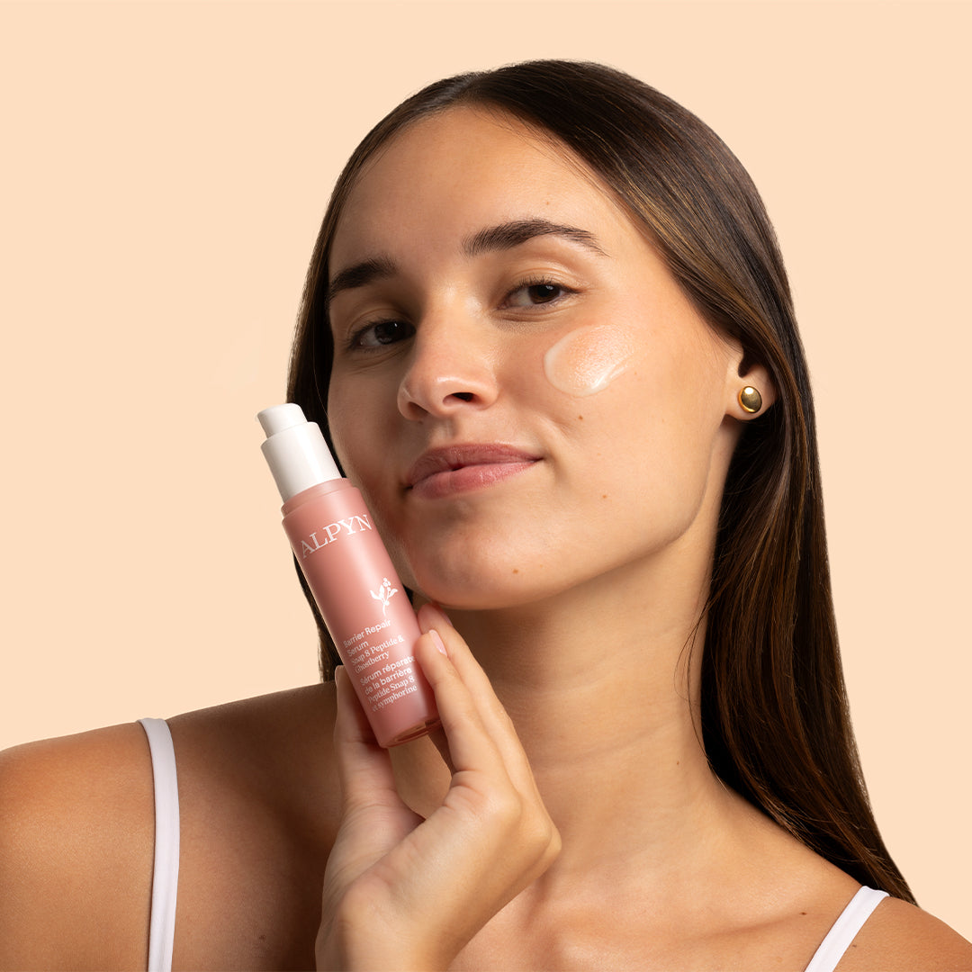 Alpyn Beauty | 3-in-1 Barrier Repair Serum | Model Image_Oct26 - woman holding serum bottle with serum applied to her cheek