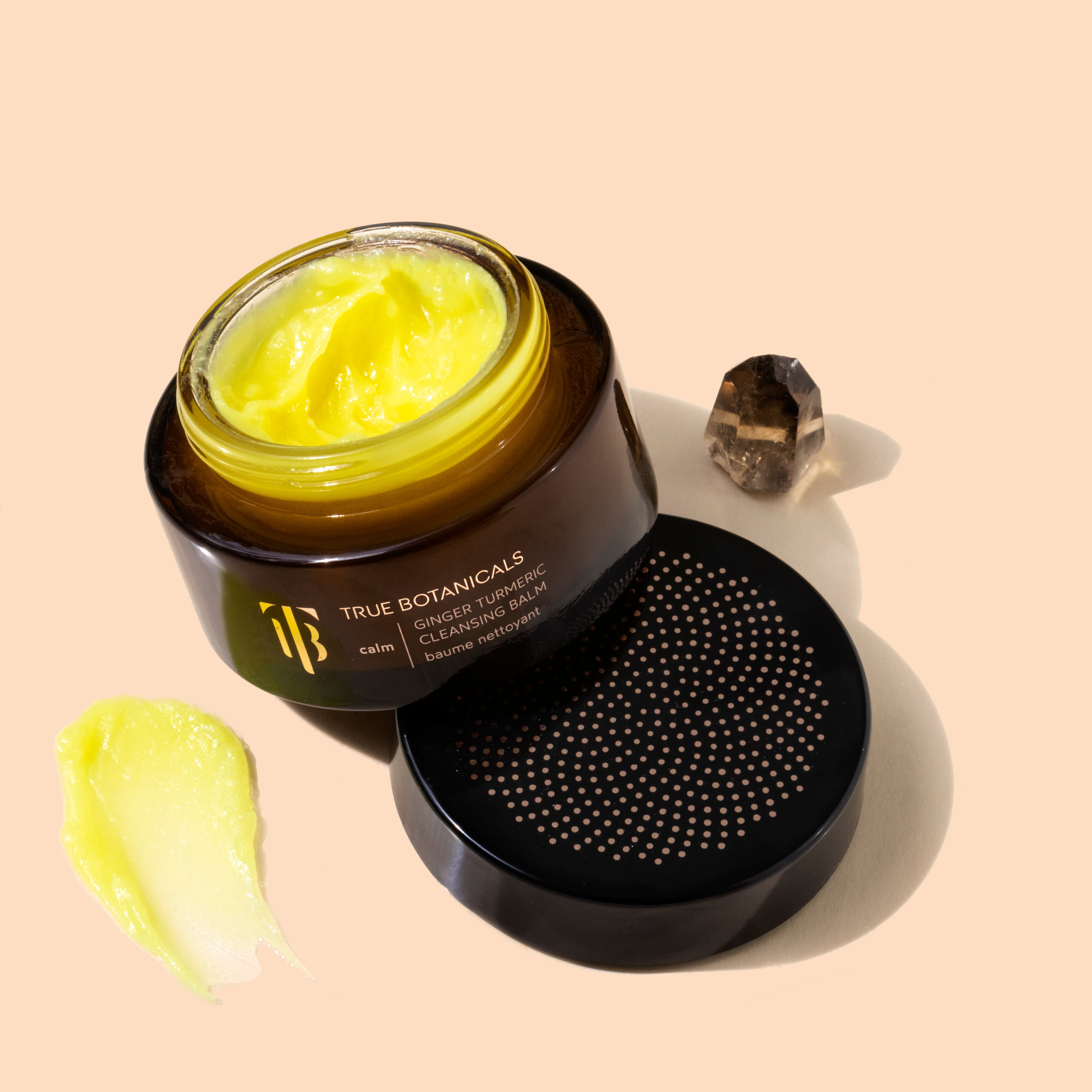 True Botanicals | Ginger Turmeric Cleansing Balm | Styled with swatch - brown jar with lid open, yellow balm inside with swatch on peach background