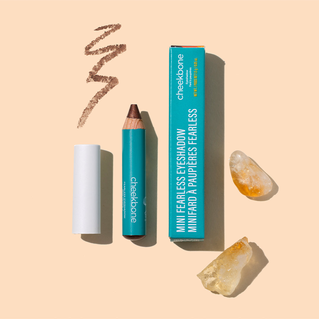 Cheekbone Beauty | Fearless Eyeshadow Mini | Styled Image with Swatch - mini pencil with teal packaging, swatch, and crystals on a peach background