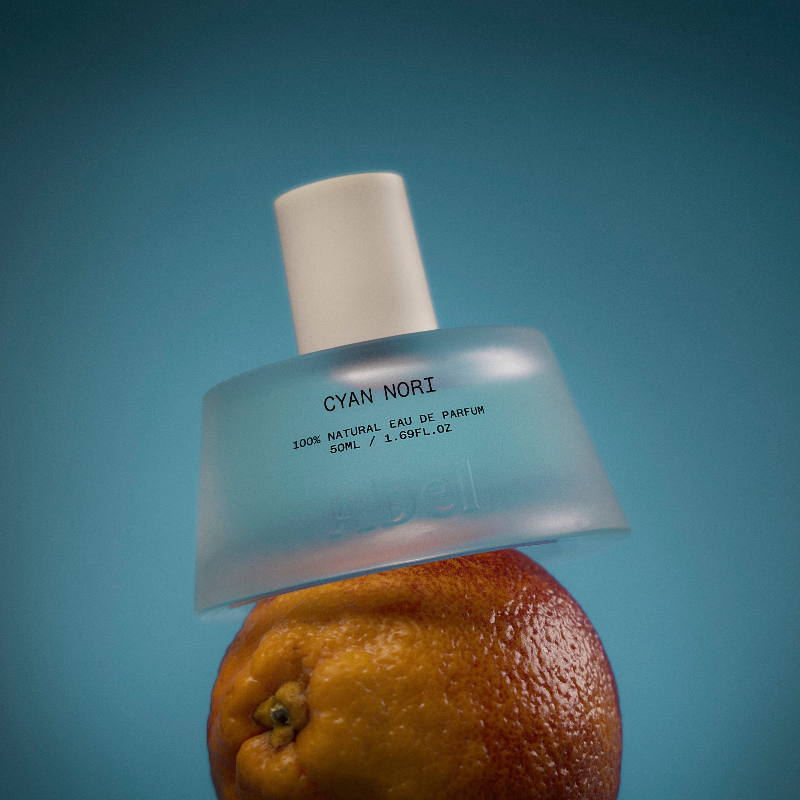 Abel | Cyan Nori Eau De Parfum | Styled image of glass bottle with white top on citrus fruit with a blue background