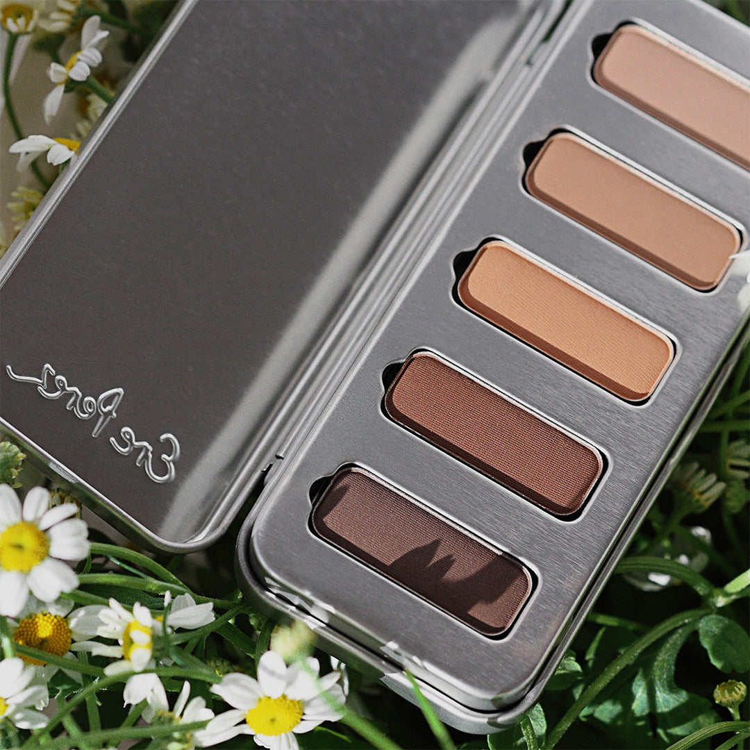 Ere Perez | Chamomile Eye Palette Element Matte | Lifestyle Image - open silver eye palette nestled among white chamomile flowers, displaying five neutral eyeshadow shades