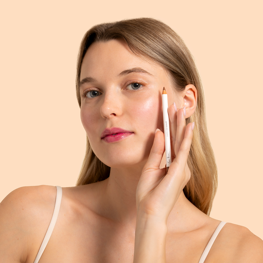 Ere Perez | Jojoba Eye Pencil | Model Image - woman holding an eye pencil near her cheek against a beige background