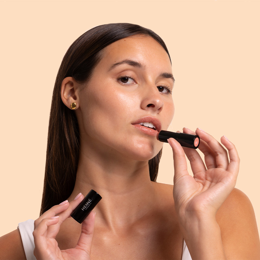 Henné | Luxury Lip Tint in Bare | Model Image - model applying lip tint against a peach background