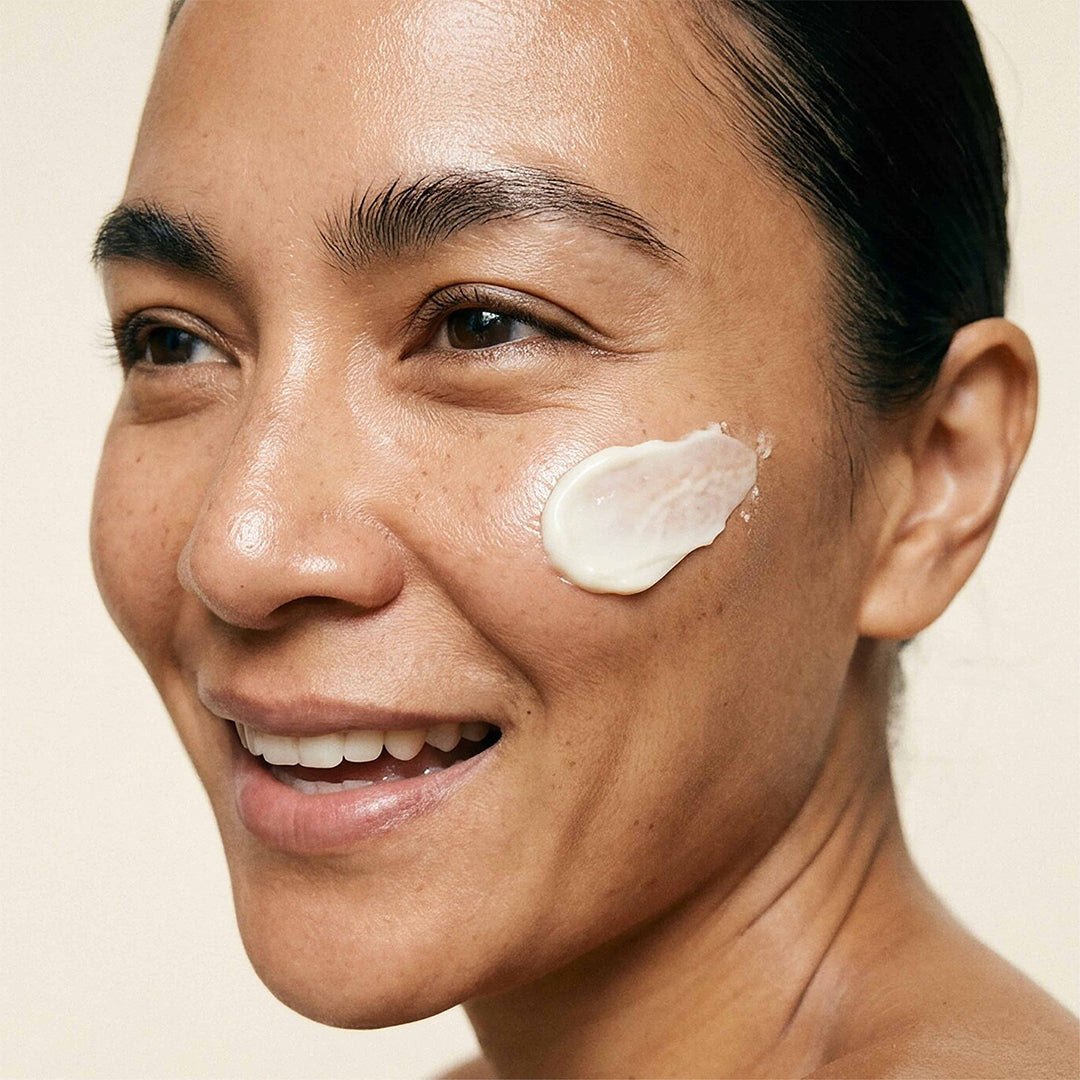 Indie Lee | Barrier Boost Moisture Cream | Model with Swatch - close-up of a smiling person with cream on the cheek