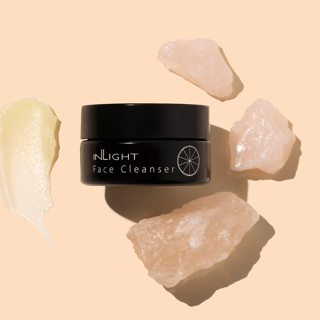 Inlight | Face Cleanser | Styled Image with Swatch_Oct26 - black jar with a pale cream product swatch and blush-pink crystals on a peach background