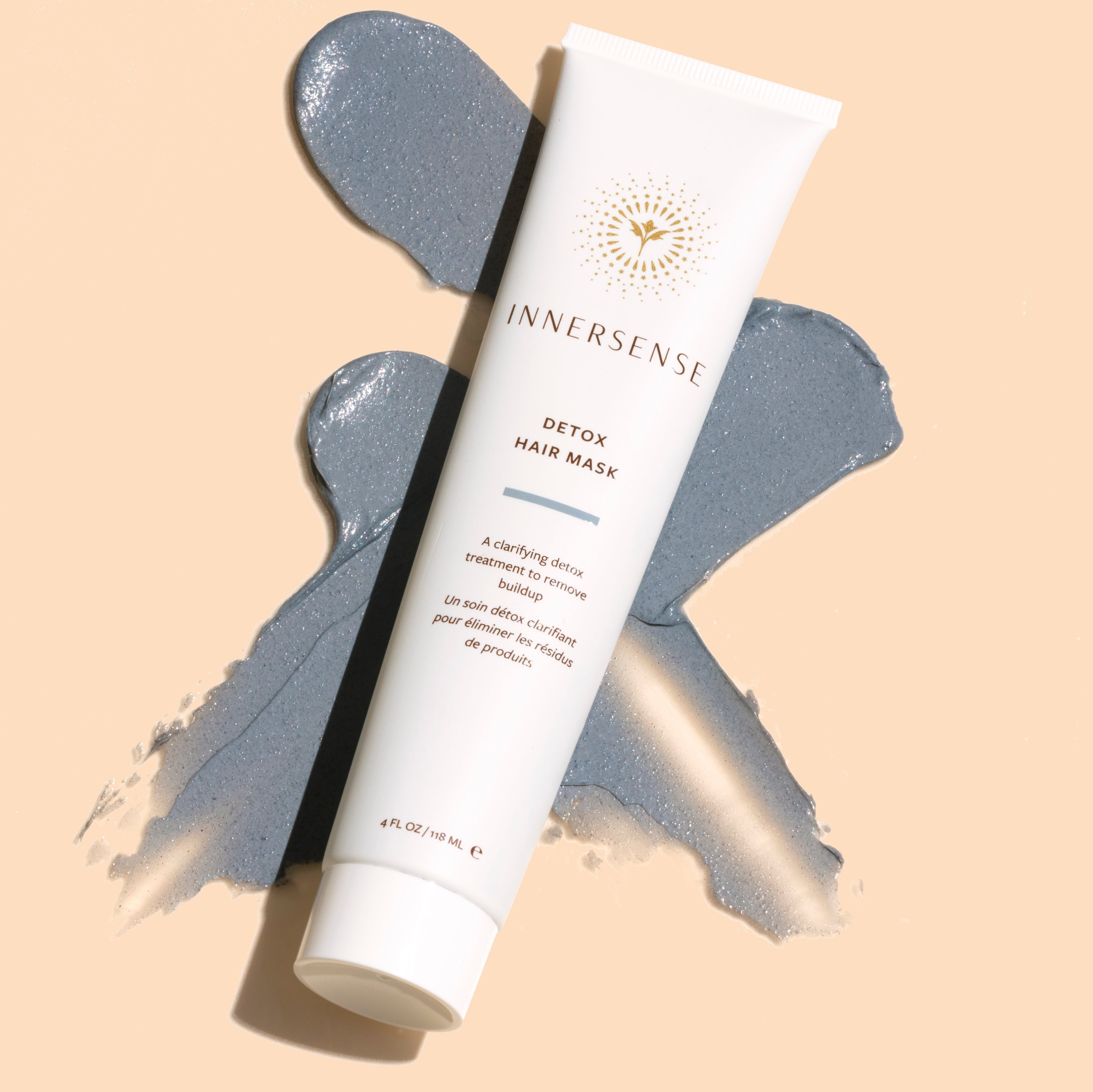 Innersense Organic Beauty | Detox Hair Mask | Styled Image with Swatch_Aug26 - white tube displayed over gray clay-like product smears on a light beige background