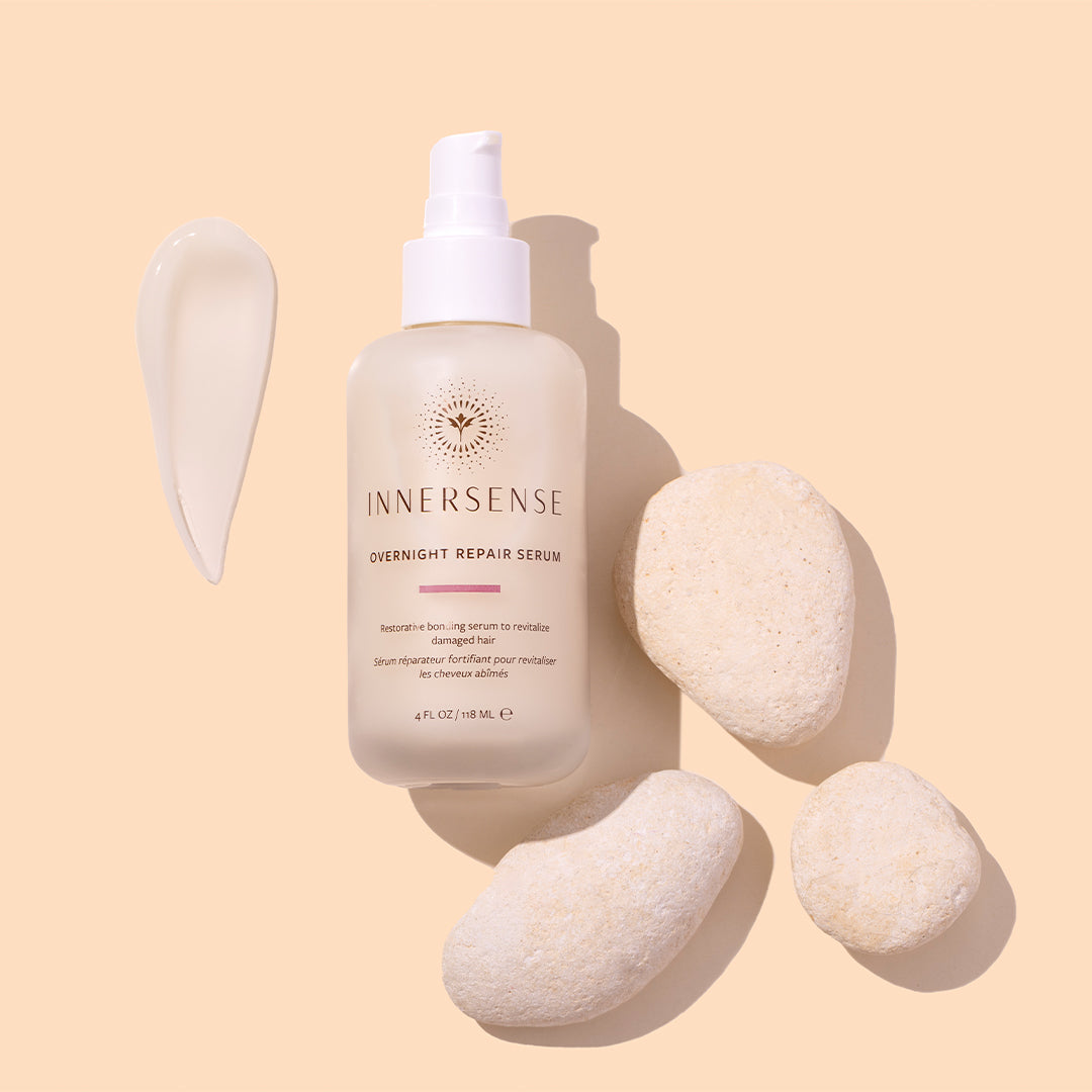 Innersense Organic Beauty | Overnight Repair Serum | Styled Image with Swatch - bottle displayed with a white cream swatch and smooth white stones on a soft beige background