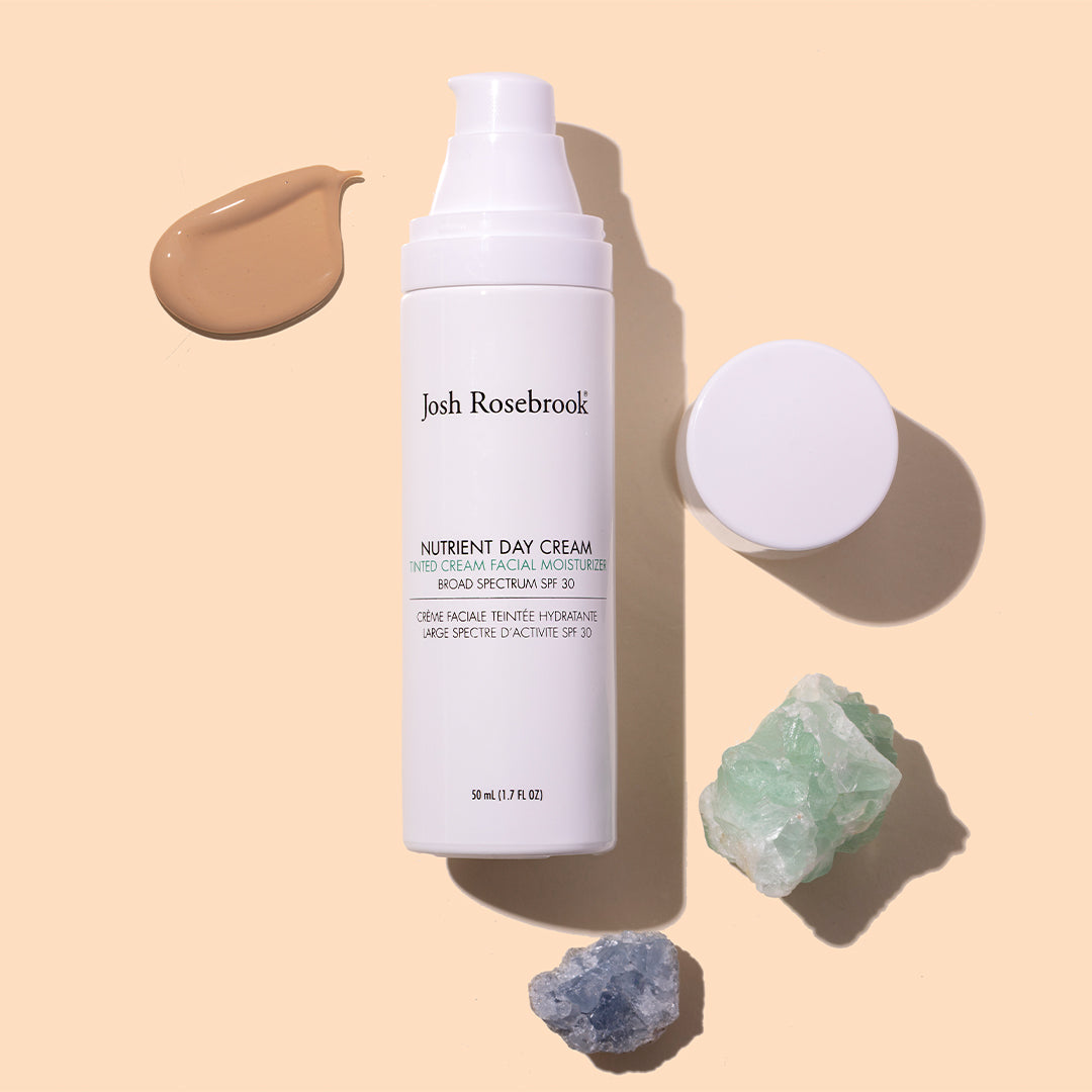 Josh Rosebrook | Tinted Nutrient Day Cream SPF 30 | Styled Image with Swatch_Jul26 - white bottle with beige cream swatch, cap, and crystals on a beige background