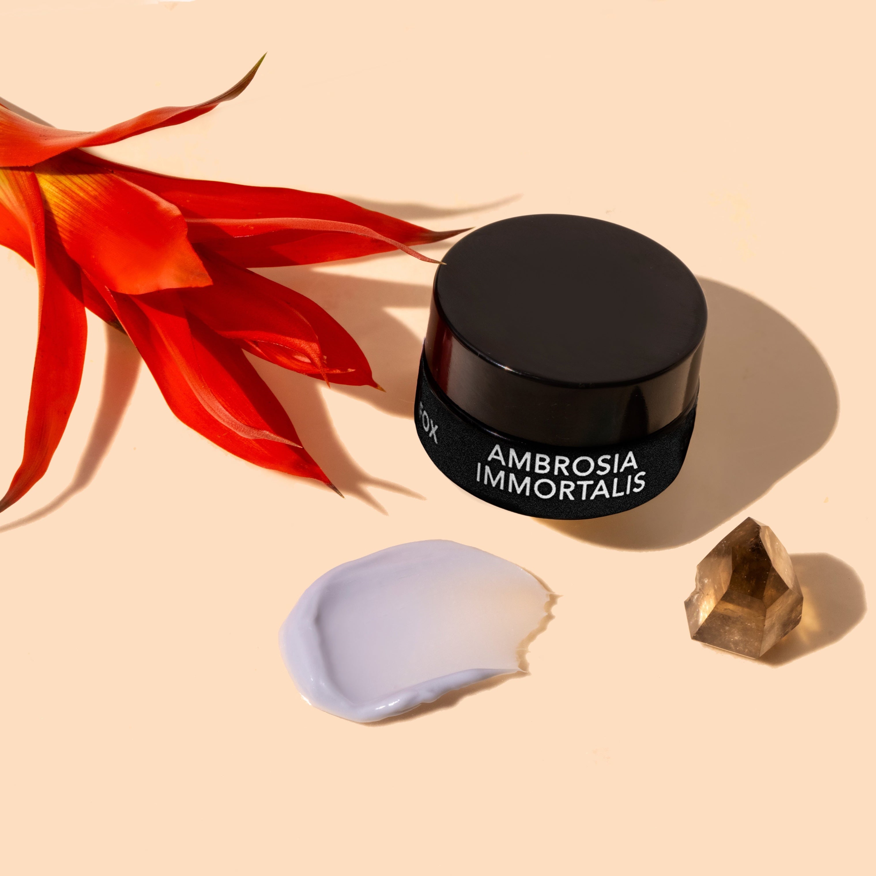 Black jar labeled 'Ambrosia Immortalis' with a red flower and crystal on a beige background