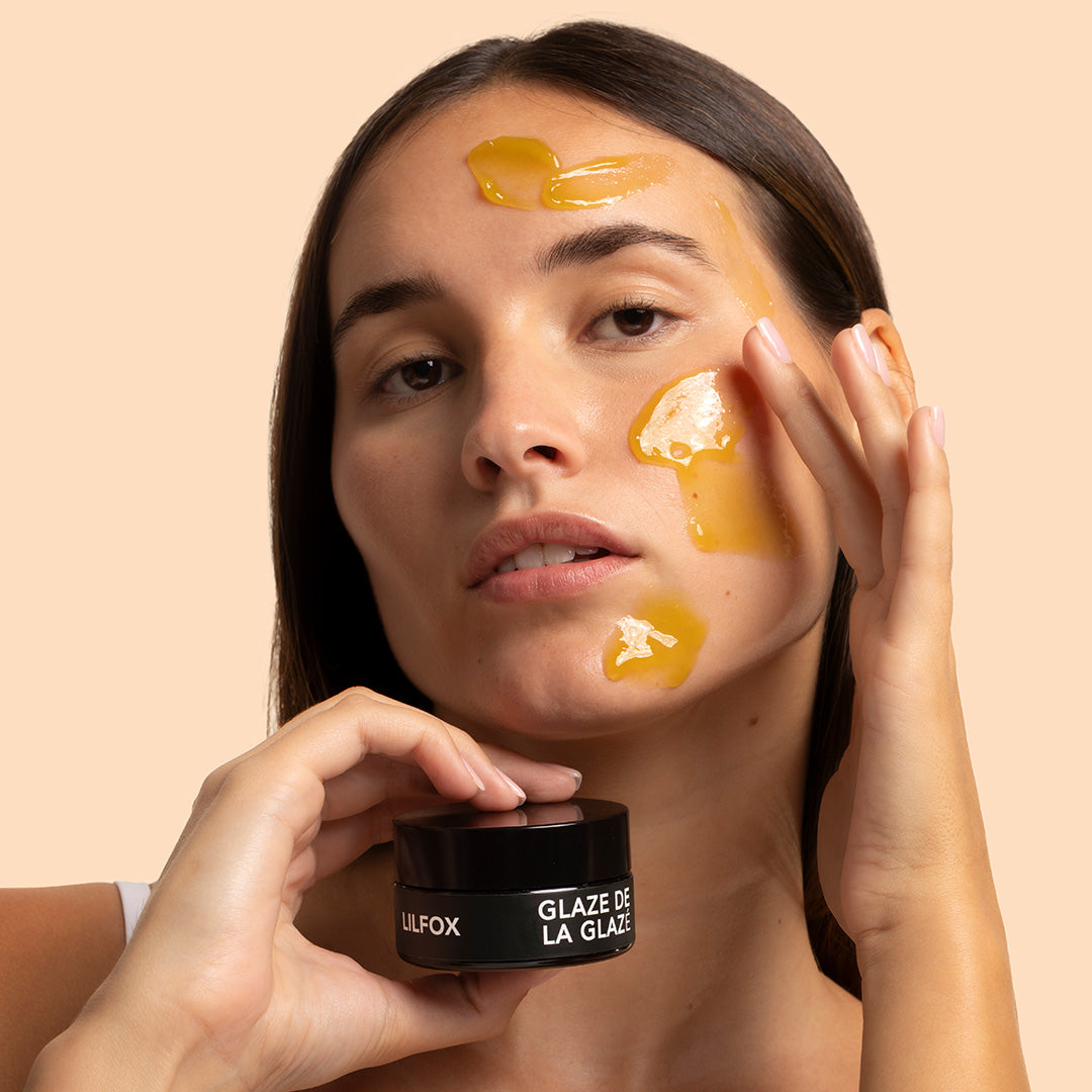 LILFOX | Glaze de la Glazé | Model Image | Model applying yellow balm product to face while holding black jar against peach background
