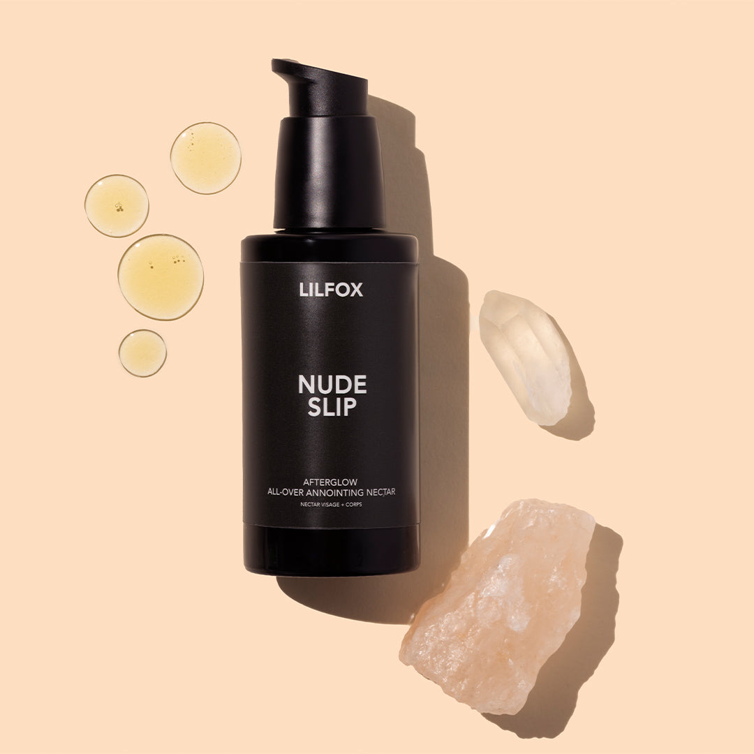 LILFOX | Nude Slip | Styled Image with Swatch_Oct26 - black pump bottle with pale yellow oil droplets and blush-pink crystals on a peach background