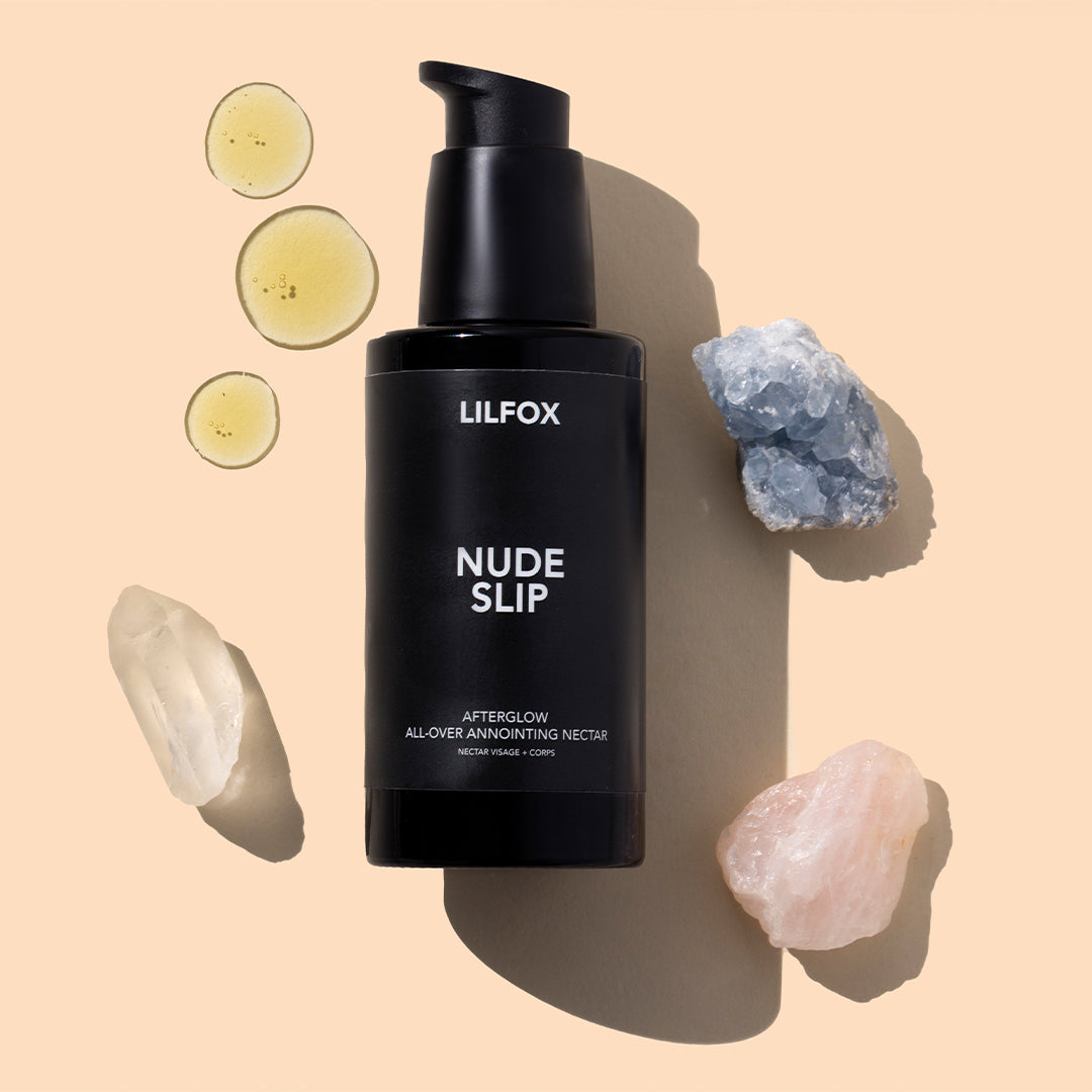 LILFOX | Nude Slip | Styled Image with Swatch_Sep26 - black pump bottle surrounded by pale blue, clear, and pink crystals with golden oil drops on a peach background