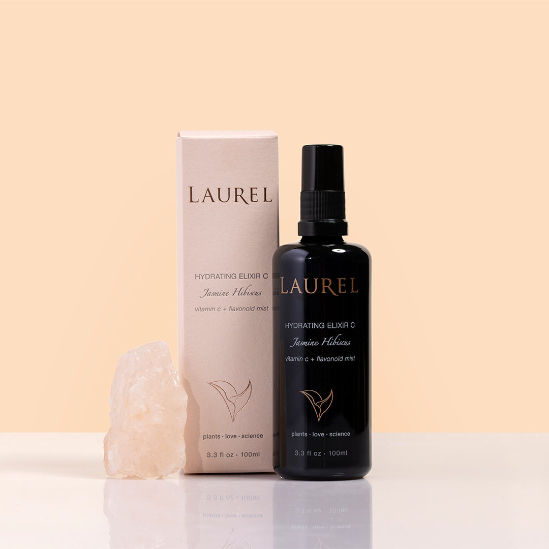 Laurel Skin | Hydrating Elixir C Jasmine Hibiscus | Packaging Image - black bottle displayed beside its box and a rose quartz crystal on a beige background
