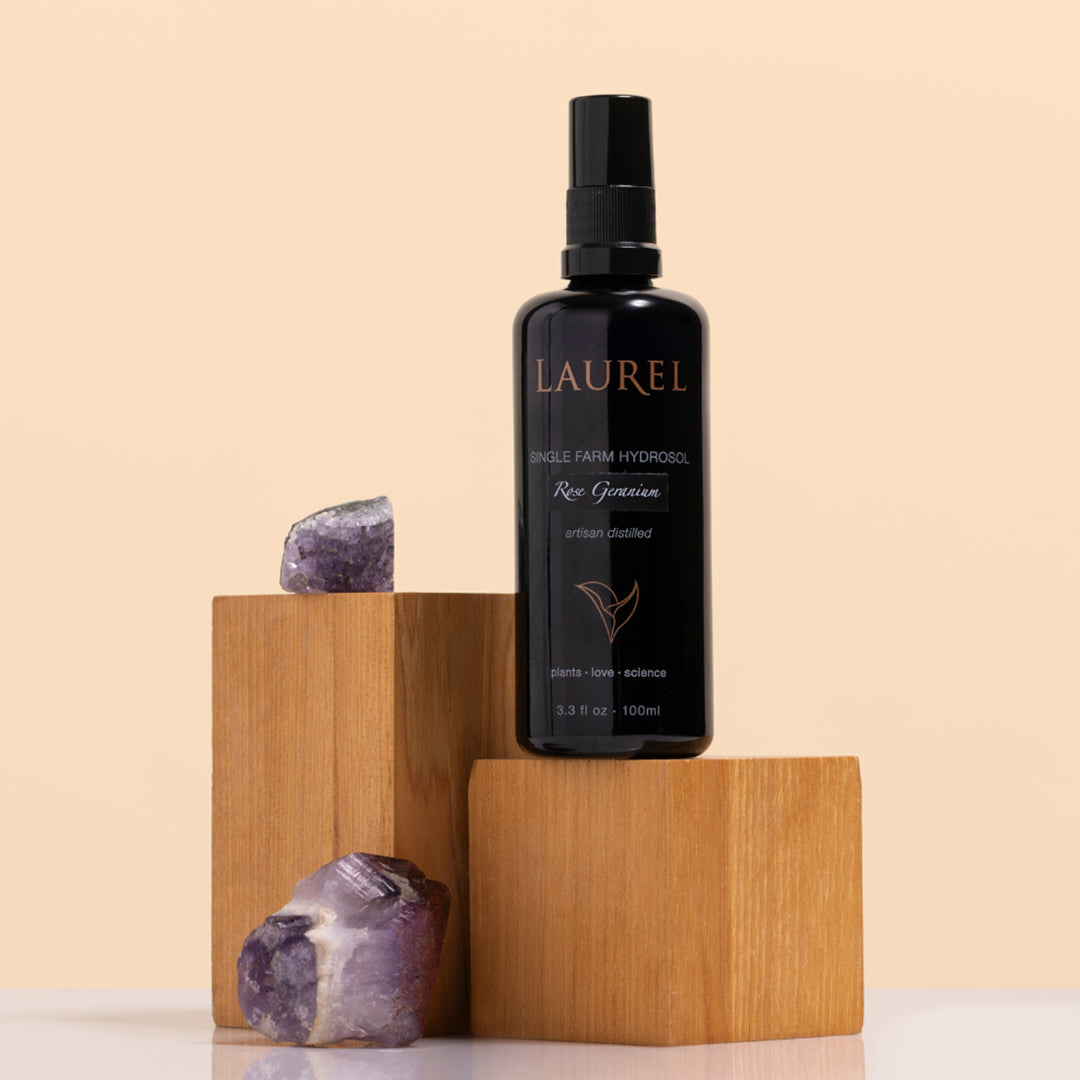 Laurel Skin | Rose Geranium Single Farm Hydrosol | Styled Image - spray bottle on wooden blocks with purple crystals on a beige background