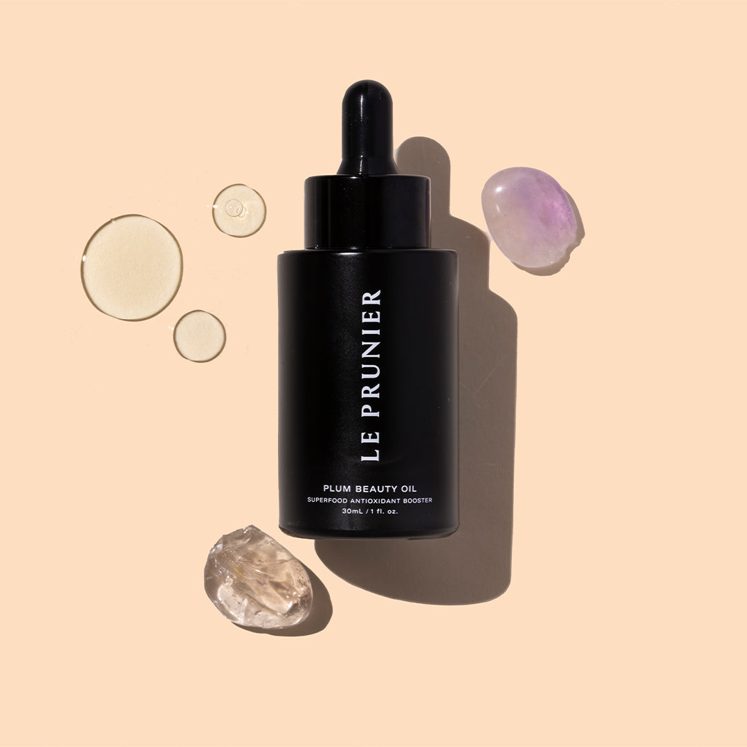 Le Prunier | Plum Beauty Oil | Styled Image with Swatch_Jul26 - black dropper bottle with oil droplets and crystals on a beige background