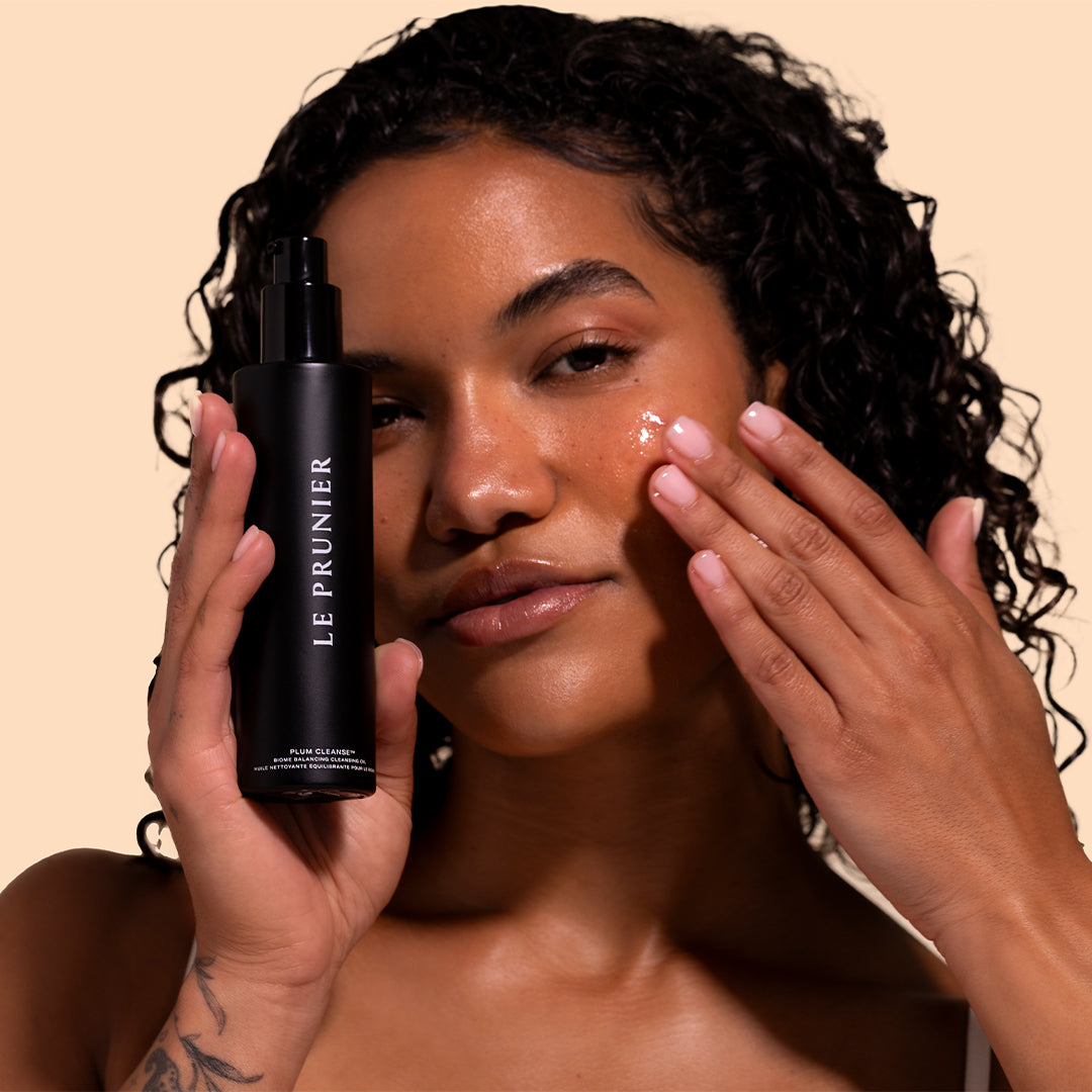 Le Prunier | Plum Cleanse | Model Image_Jul26 - Model holding bottle while applying the cleanser to the cheek