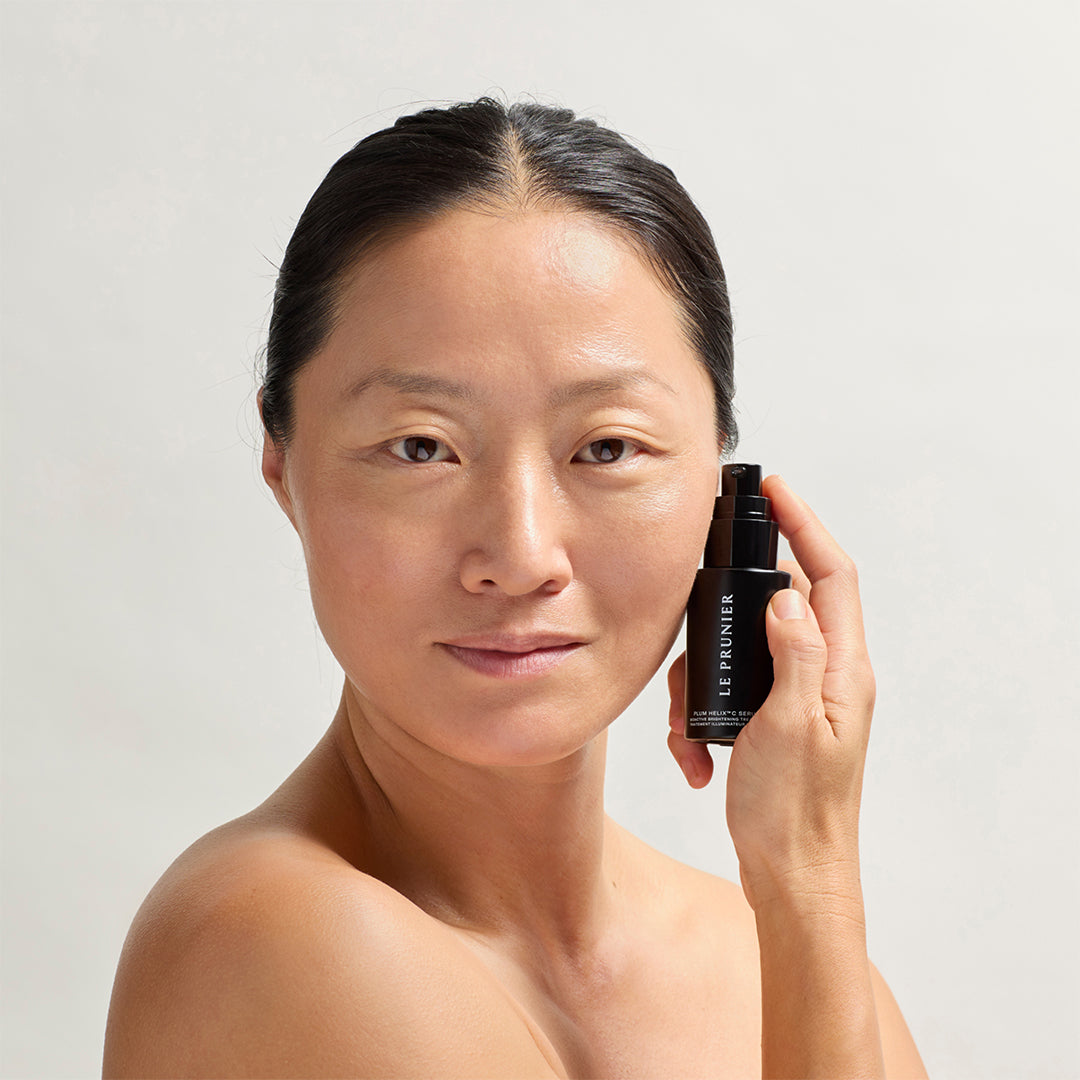 Le Prunier | Plum Helix C Serum | Model Image - woman holding black pump bottle serum beside her face