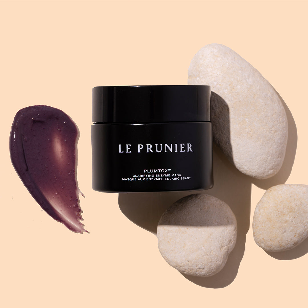 Le Prunier | Plumtox Clarifying Enzyme Mask | Styled Image with Swatch_Jul26 - jar with a purple mask swatch and white stones on a beige background