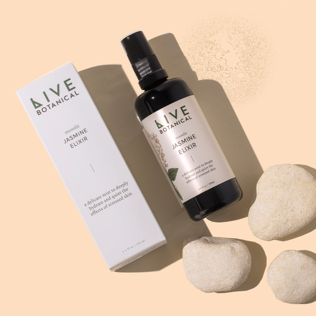 Live Botanical | Moonlit Jasmine Elixir | Styled Image with Swatch_Oct26 - black spray bottle with a white box and cream-colored stones on a peach background