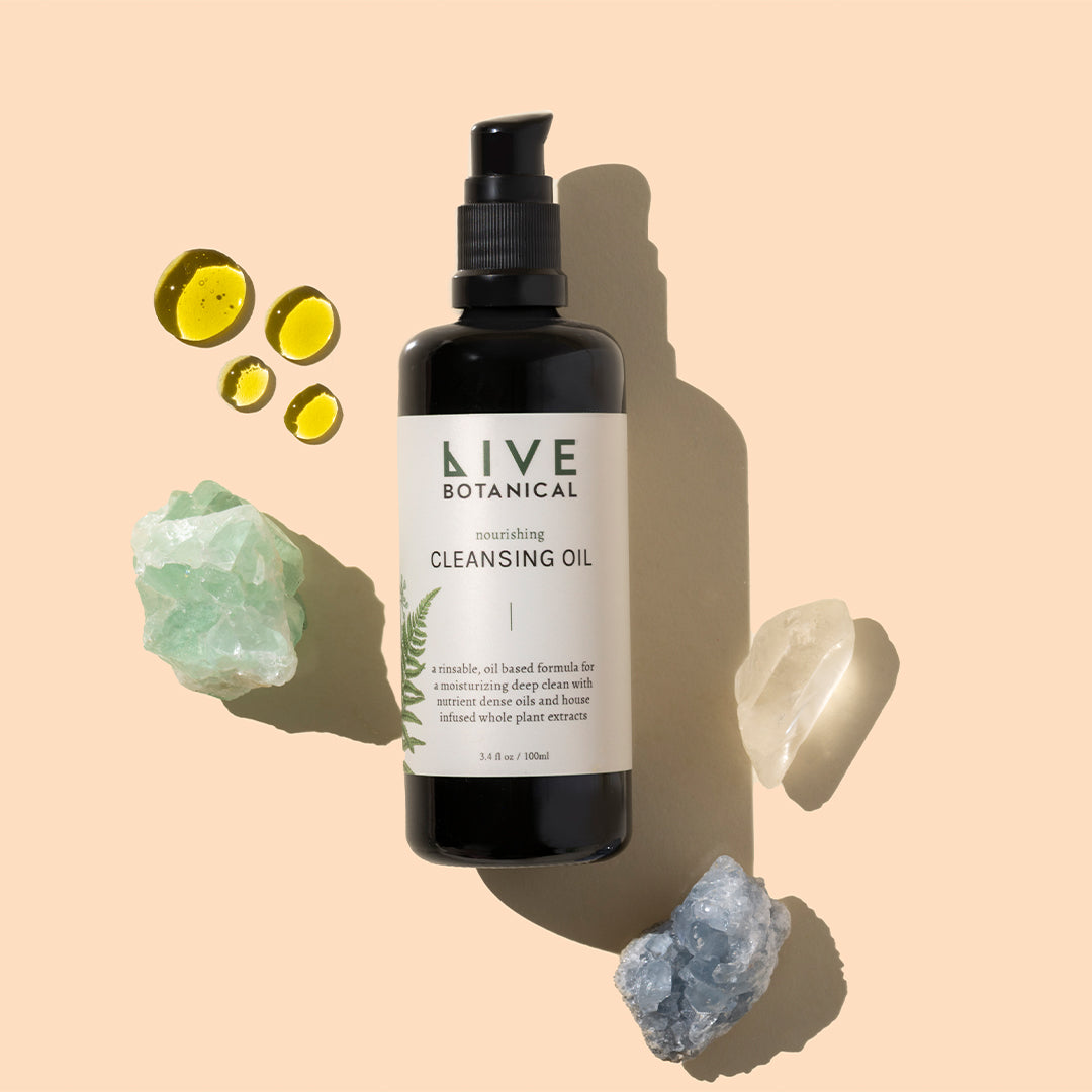 Live Botanical | Nourishing Cleansing Oil | Styled Image with Swatch_Sep26 - cleansing oil bottle with oil swatches, crystals, and stones on a peach background