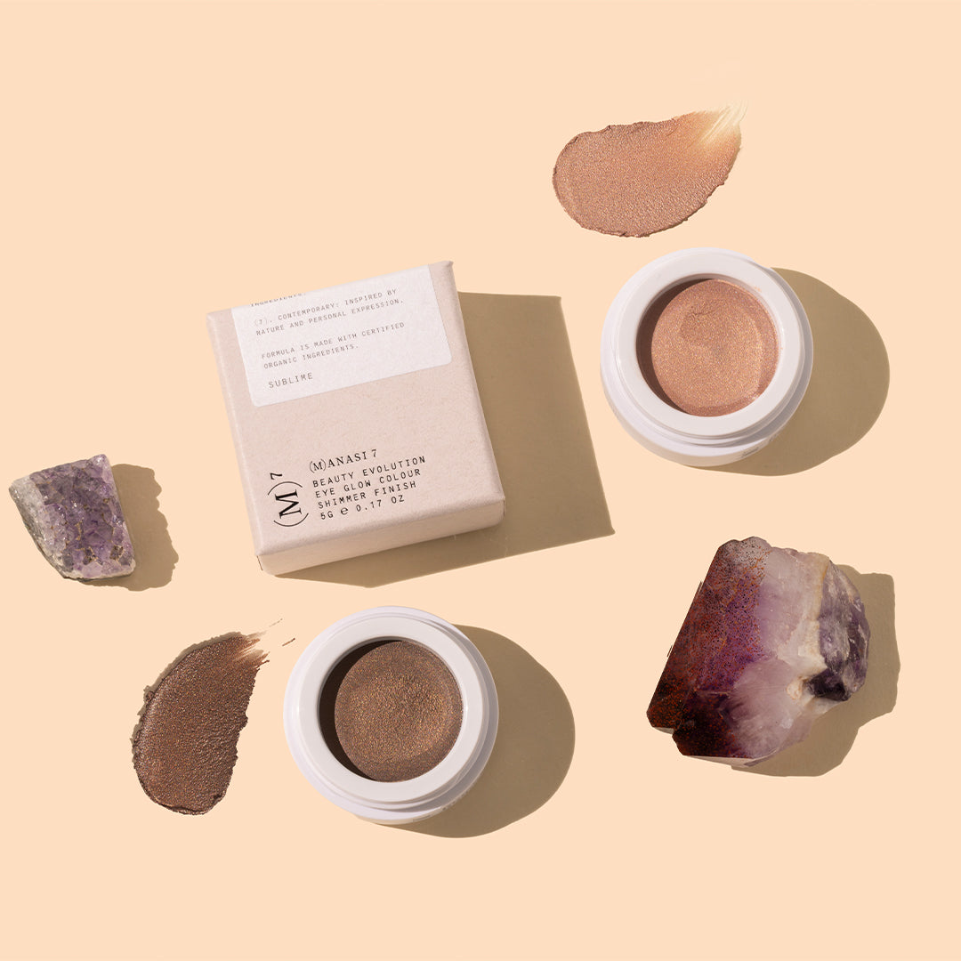 Manasi 7 | Eye Glow Colour | Styled Image with Swatch_Oct26 - shimmery bronze, taupe-brown, and copper-toned eye colors with matching swatches, white packaging, beige box, and purple crystals on a warm peach background