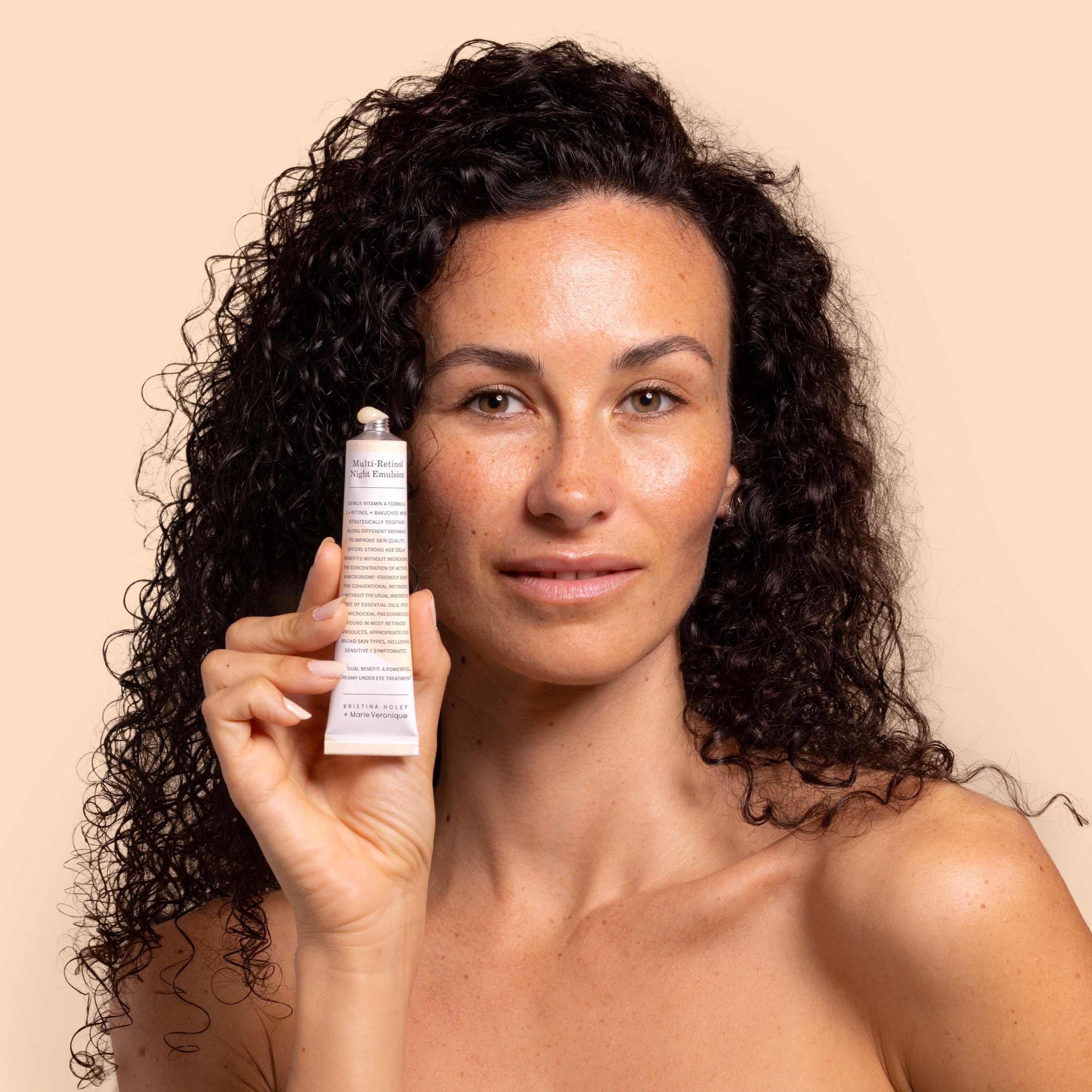 Woman holding Marie Veronique Multi Retinol Night Emulsion tube in front of beige background