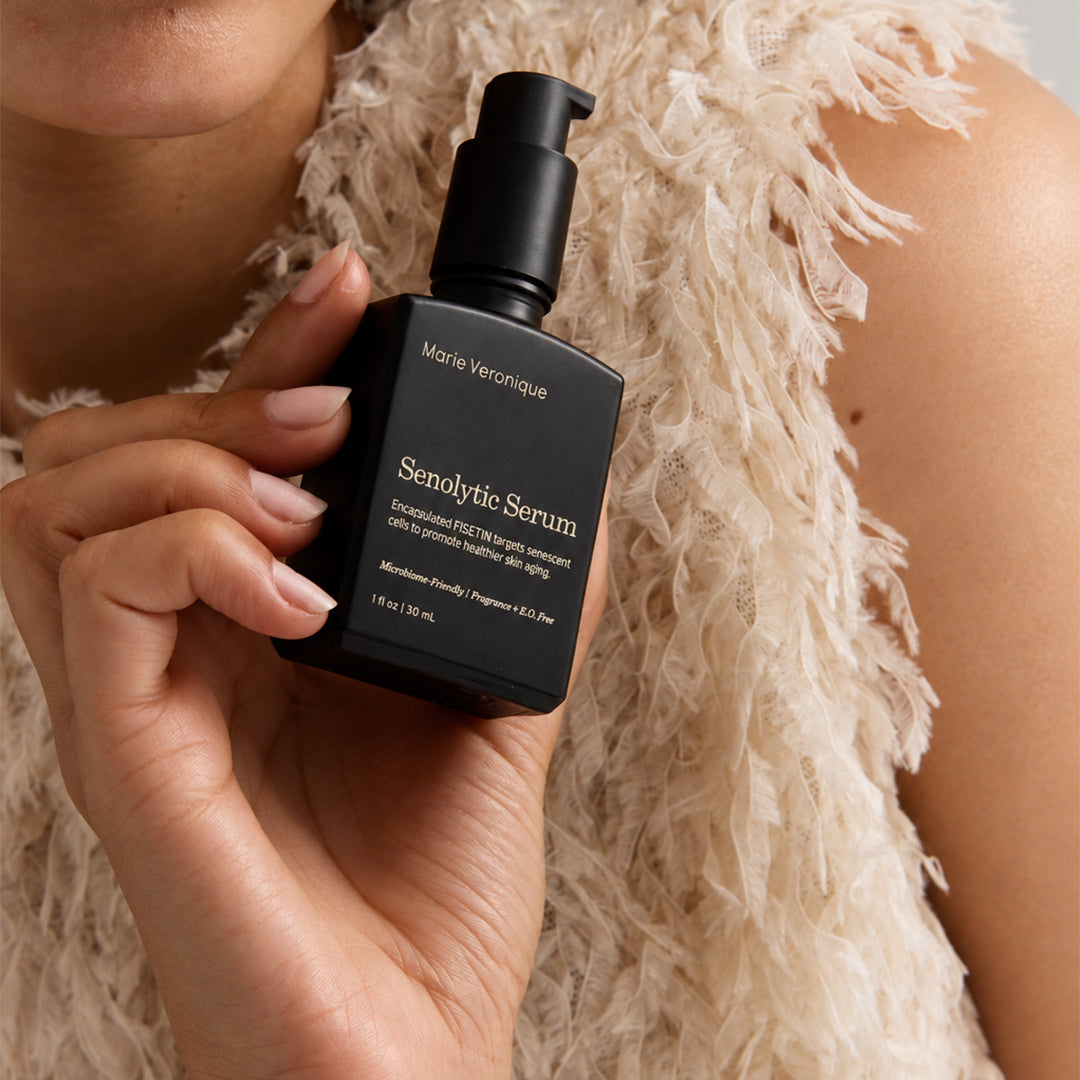 Marie Veronique | Senolytic Serum | Model Image - model holding a bottle of serum against a textured cream top