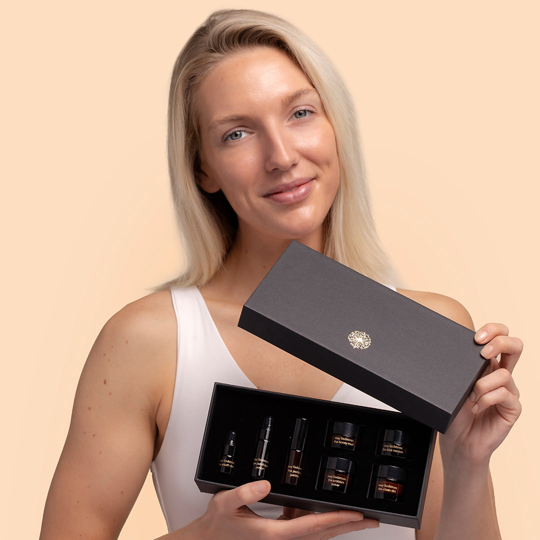 May Lindstrom Skin The Chocolate Box, model holding, model on peach background holding black gift box with small product bottles inside