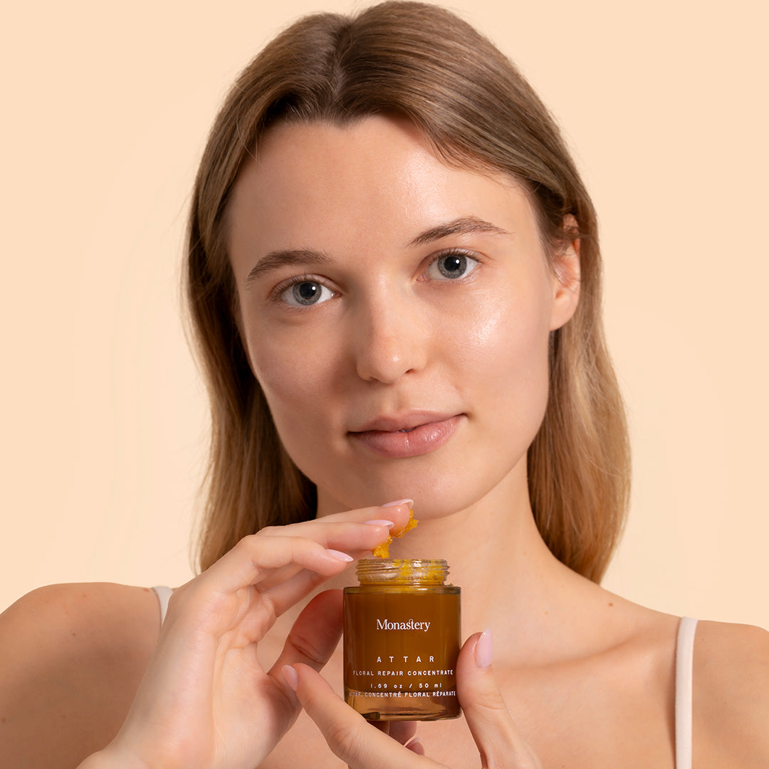 Monastery | Attar | Model with product | women holding brown jar with yellow balm product on fingers