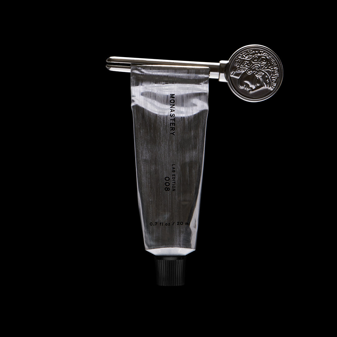 Monastery | Universal Balm | Lifestyle Image - silver tube with coin logo key on a black background
