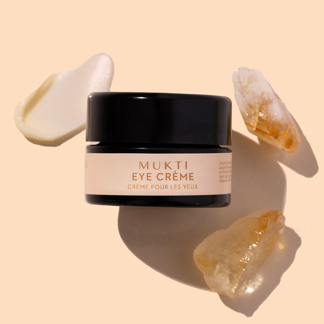 Mukti | Bioactive Renewal Eye Creme | Styled image with swatch | Black jar with white product swatch on peach background