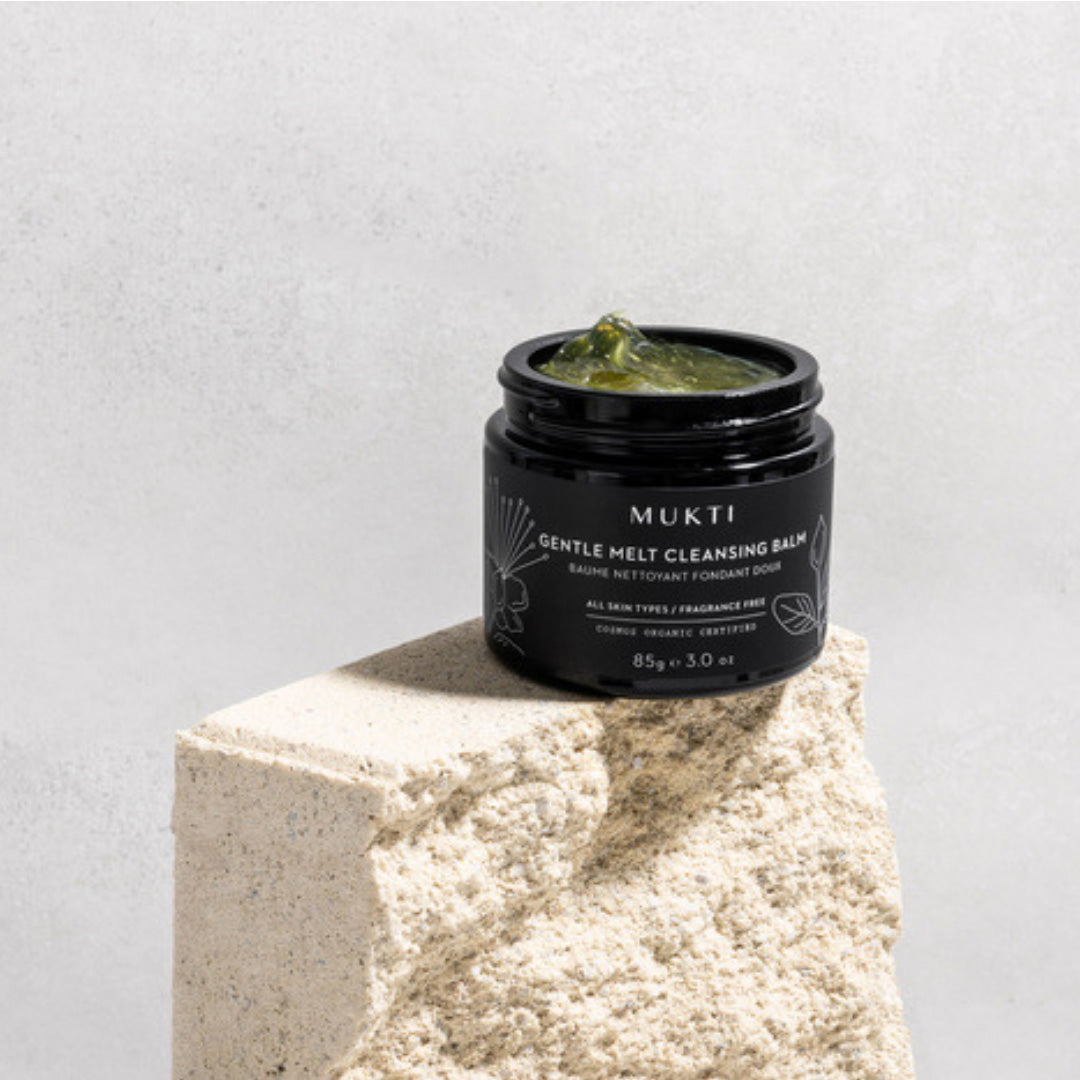 Mukti | Gentle Melt Cleansing Balm | Open Jar Image - open black jar of balm displayed on a stone pedestal