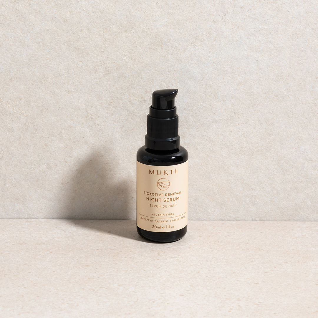 Mukti Organics | Bioactive Renewal Night Serum | Lifestyle Image - black pump bottle with beige label on a light beige textured