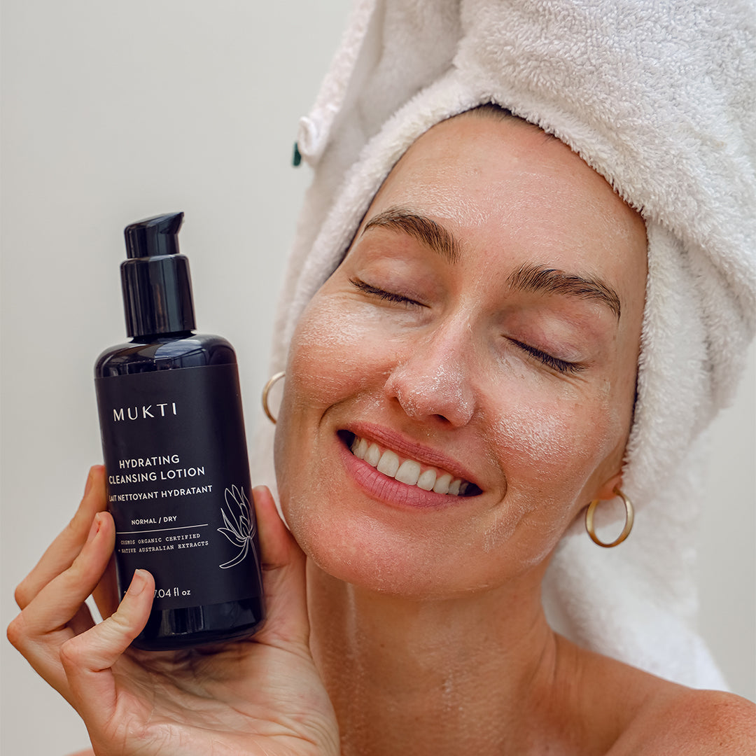 Mukti Organics | Hydrating Cleansing Lotion | Model Image - model holding cleansing lotion against a light gray background