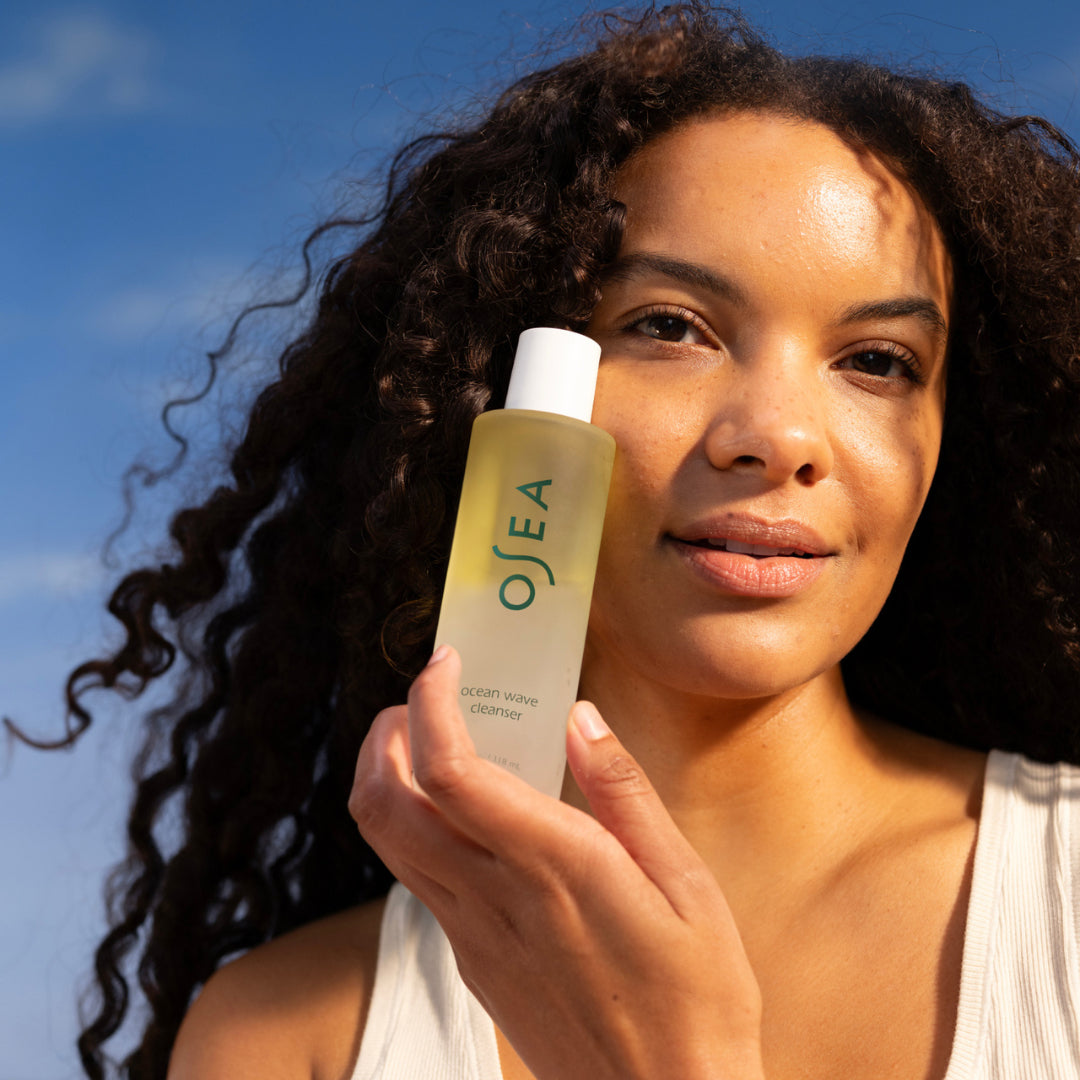 OSEA | Bi-Phase Oil Cleanser | Model Image - model holding cleanser against a blue sky background