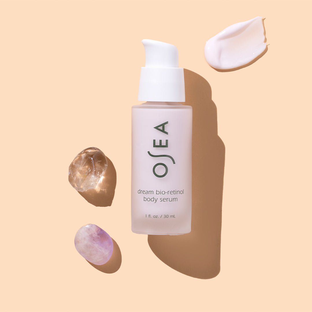 OSEA | Dream Bio-Retinol Body Serum 1 oz | Styled Image with Swatch - pump bottle displayed on a beige background with crystal accents and a soft pink serum swatch