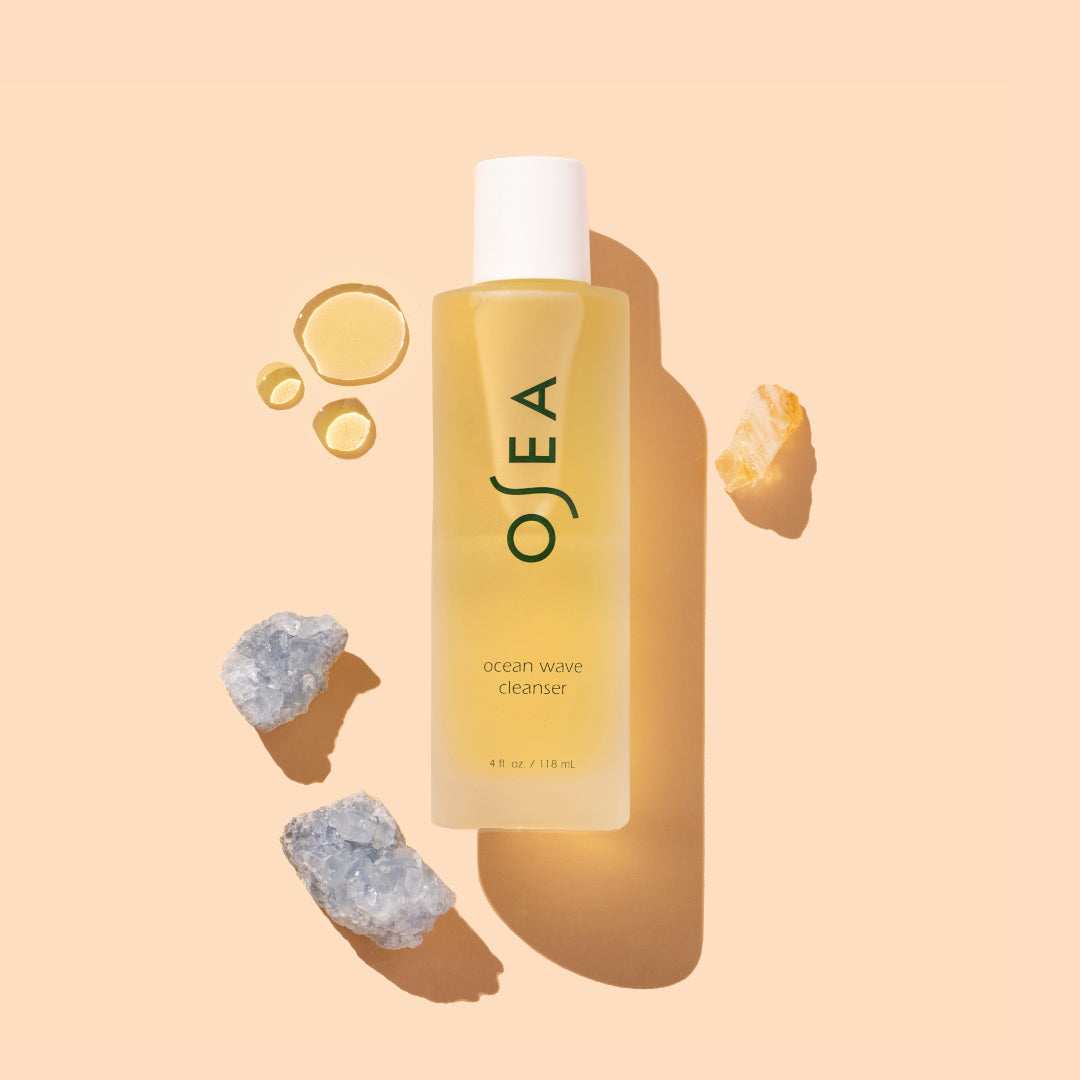 OSEA | Ocean Wave Cleanser | Product Image with Swatch - bottle with yellow gel texture drops and crystals on a warm beige background