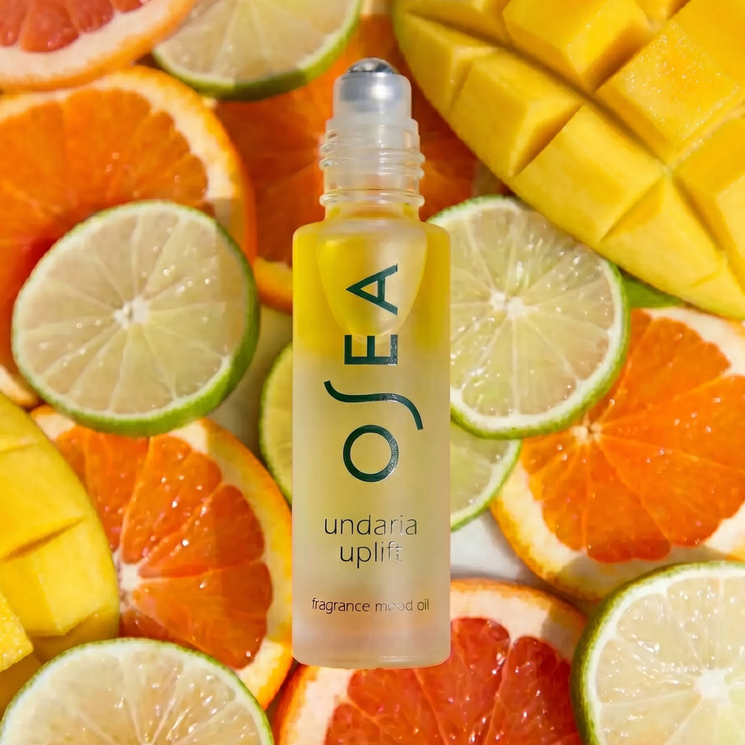 OSEA | Undaria Uplift Fragrance Mood Oil | Lifestyle Image - rollerball surrounded by grapefruit, lime, orange, and mango slices