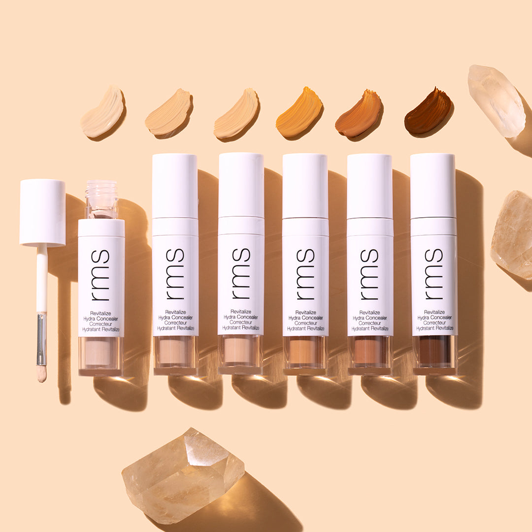 RMS Beauty | Revitalize Hydra Concealer | Product Image with Swatch - concealer lineup in multiple shades with applicator wand and swatches above on a beige background