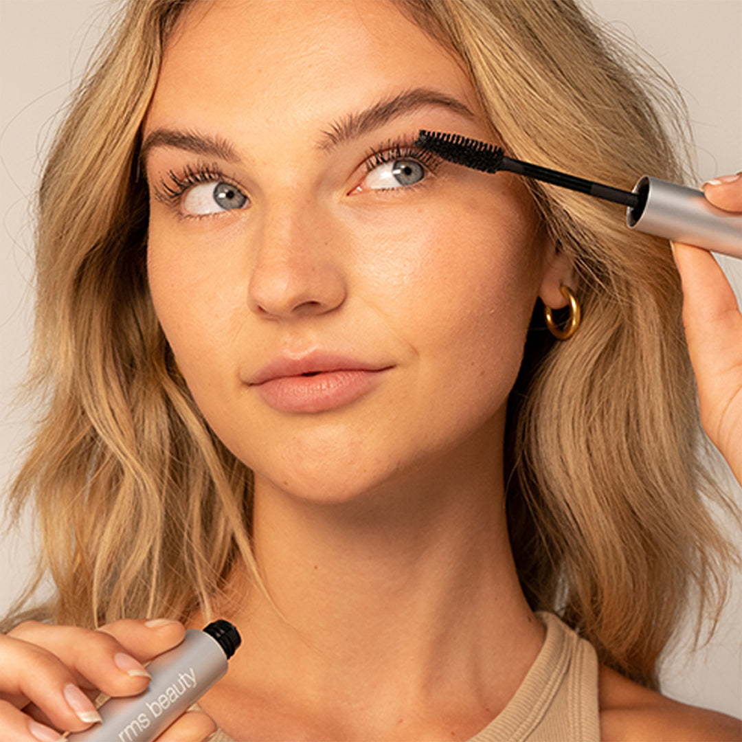 RMS Beauty | Straight Up Volumizing Peptide Mascara | Model Image - model applying mascara to her upper lashes with a black mascara wand