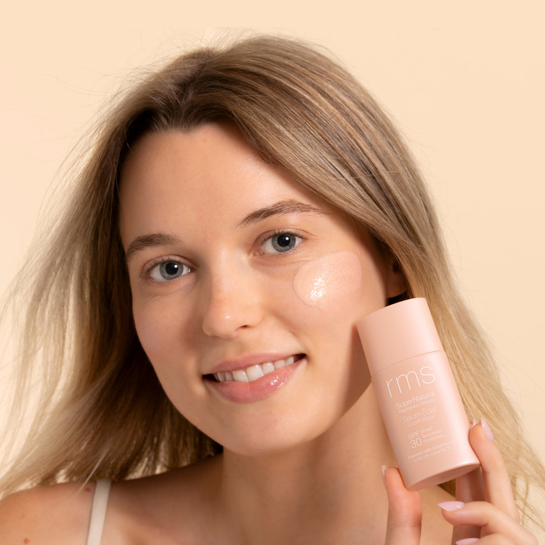 RMS Beauty | SuperNatural Radiance Serum Broad Spectrum SPF 30 Sunscreen | Model Image - woman with product applied on cheek against a neutral background