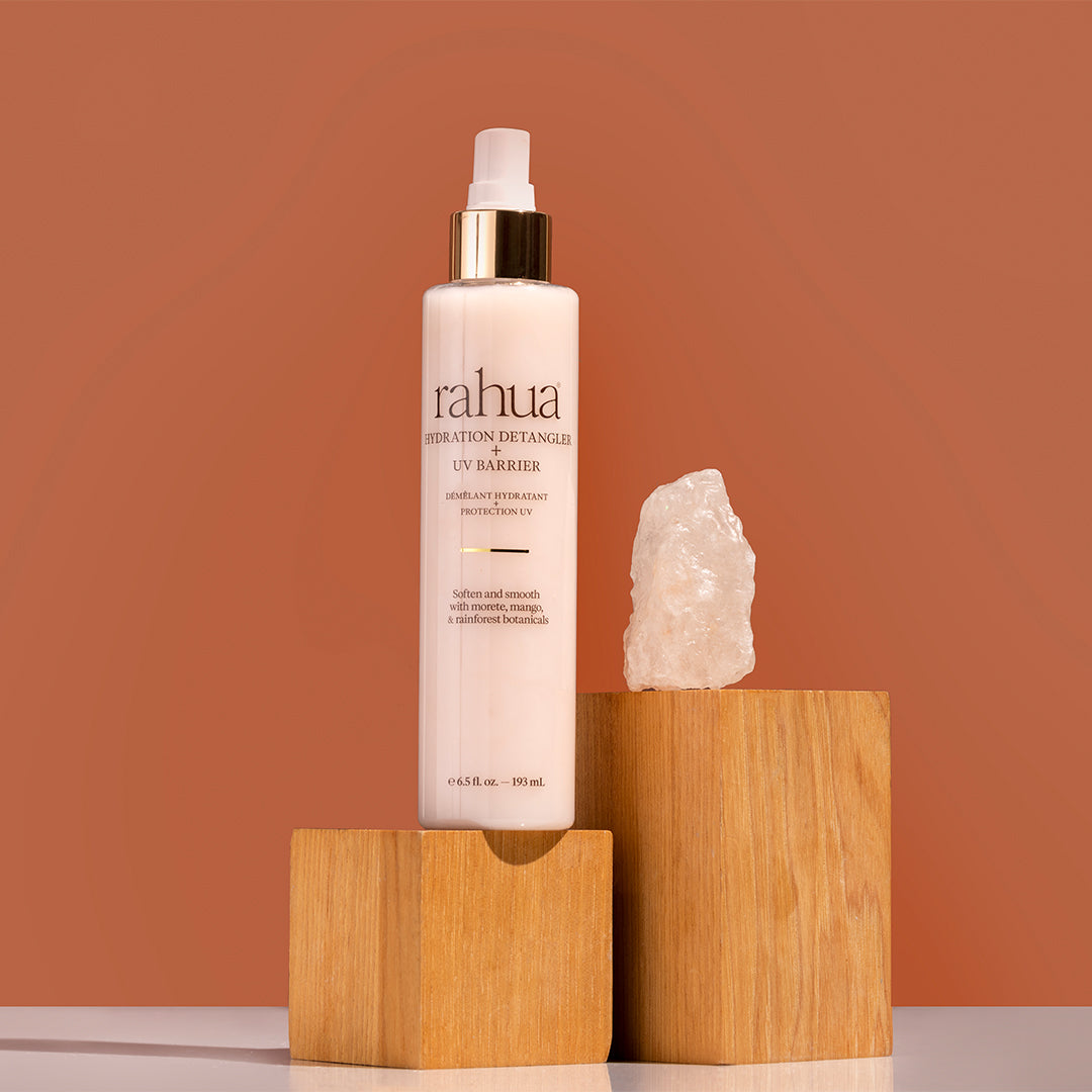 Rahua | Hydration Detangler + UV Barrier | Product Image3 - spray bottle with white and gold cap with crystals against a brown background
