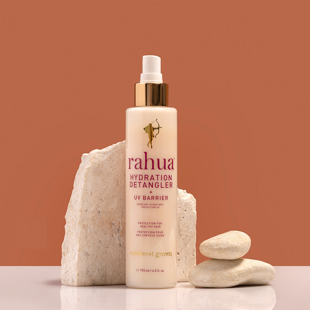 Rahua | Hydration Detangler + UV Barrier | Styled Image_Aug26 - spray bottle styled with natural stone props on a warm earth tone background