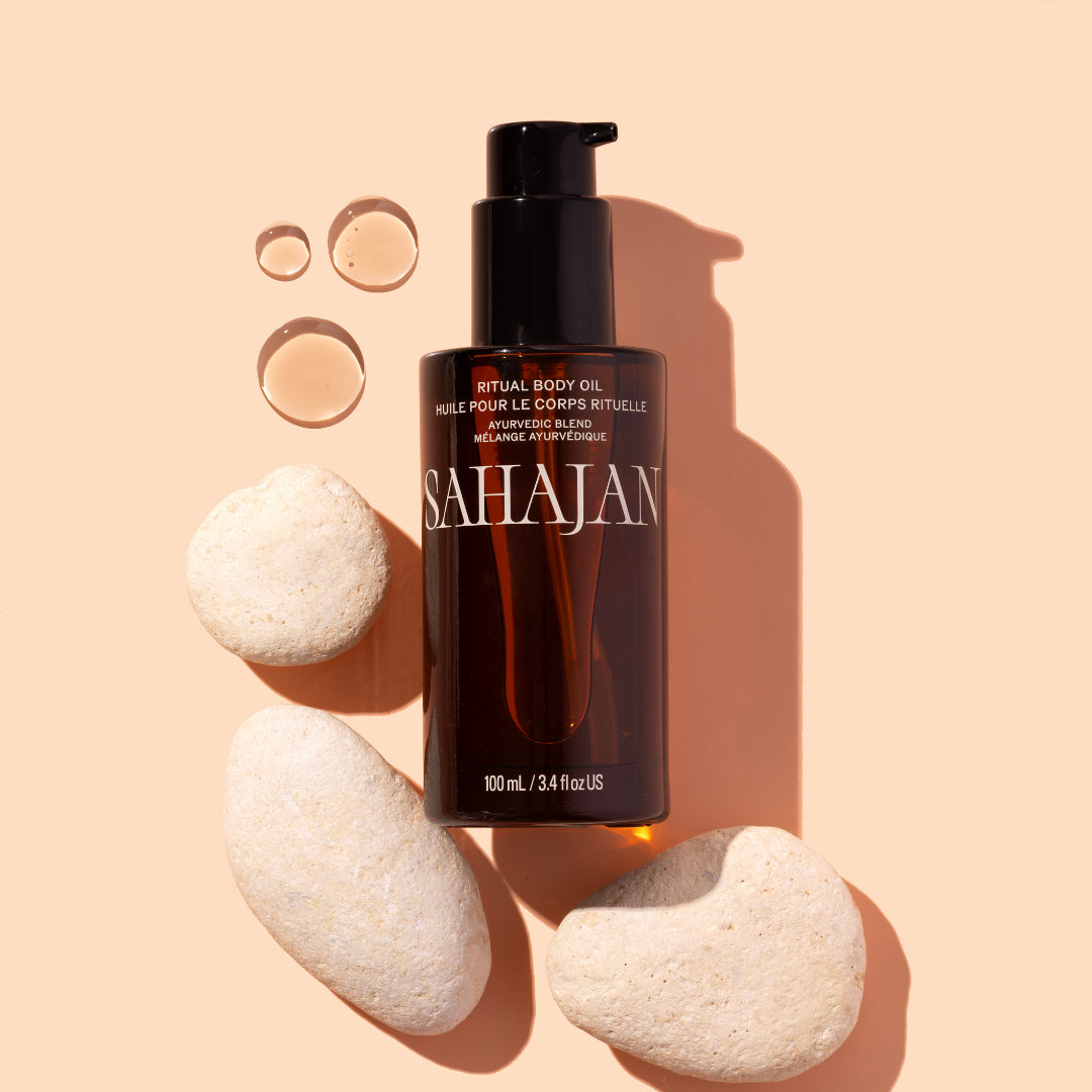 Sahajan | Ritual Body Oil | Styled Image with Swatch - bottle styled with oil droplets and smooth stones on a beige background