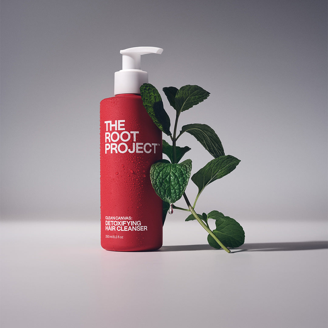 The Root Project | Clean Canvas Detoxifying Hair Cleanser | Lifestyle Image - red pump bottle with green leaves on a gray background