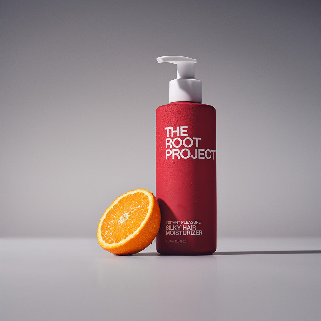 The Root Project | Instant Pleasure Silky Hair Moisturizer | Lifestyle Image - red pump bottle beside a sliced orange on a gray background