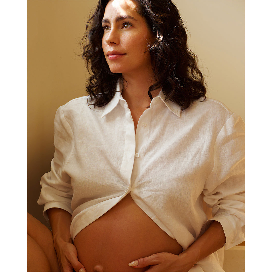 True Botanicals | Mindful Mama Belly & Body Oil | Pregnant Model Image1 - pregnant person in a white shirt gently holding their belly